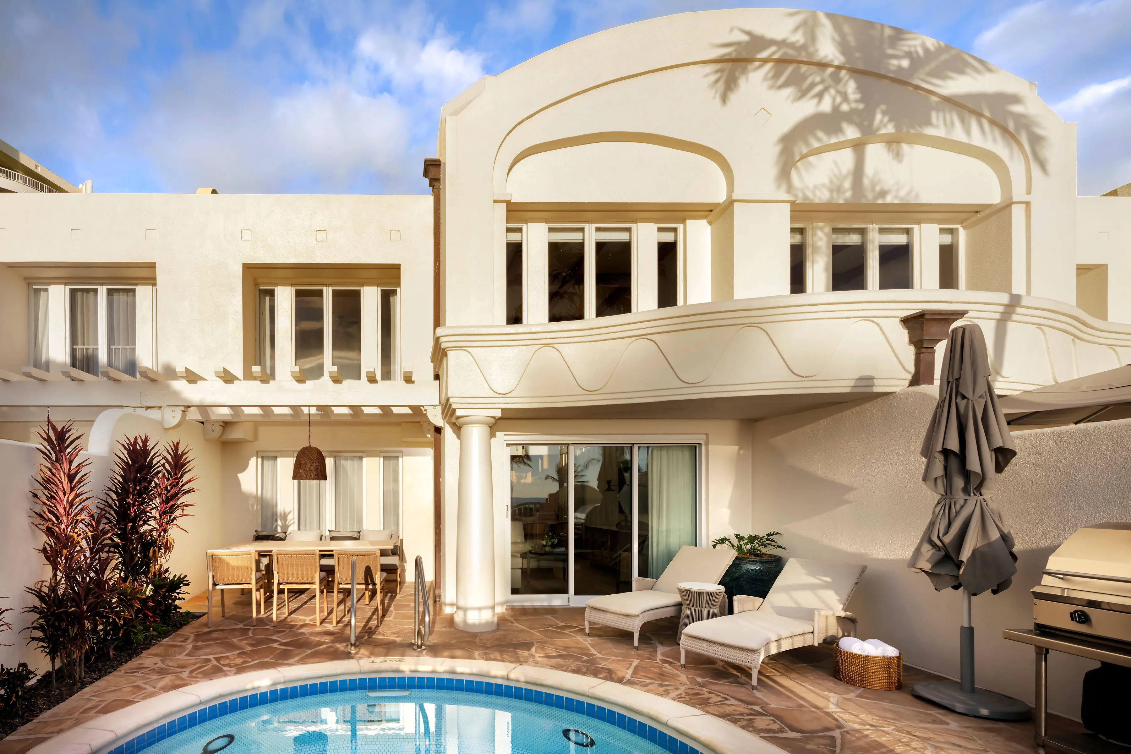 The exterior of Villa Lanaiin at Fairmont Kea Lani featuring a tiled terrace with loungers and outdoor dining table, a balcony, and a glimpse of a pool