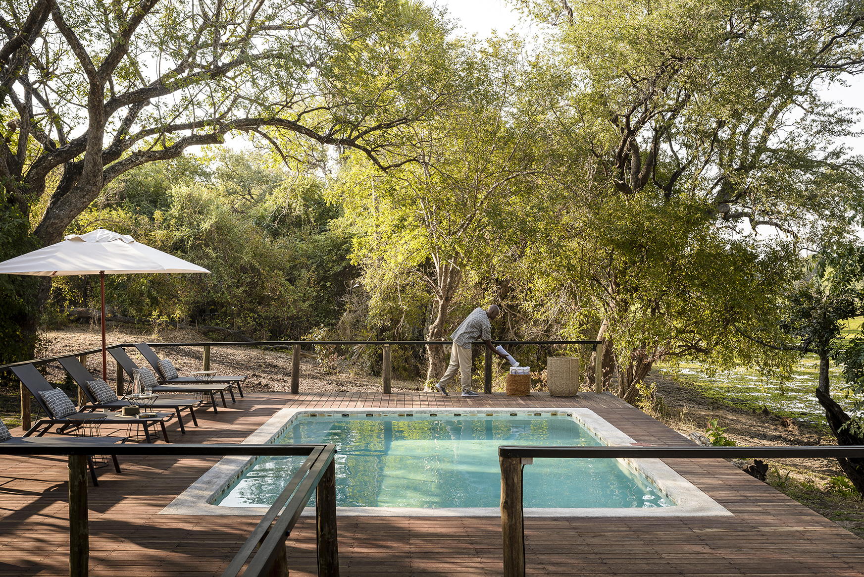 Africa, Zambia, Sugani Lodge, man placing towels beside the main pool and sunloungers