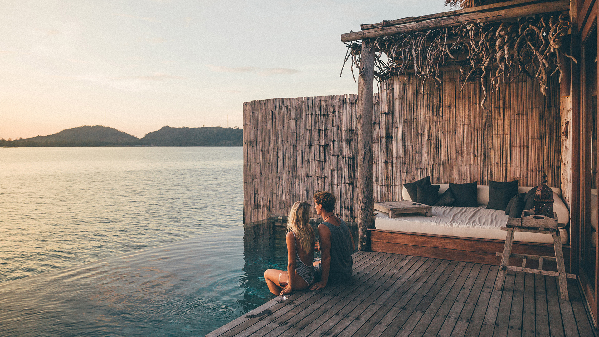 A couple sat on the edge of an infinity pool on an over water villa