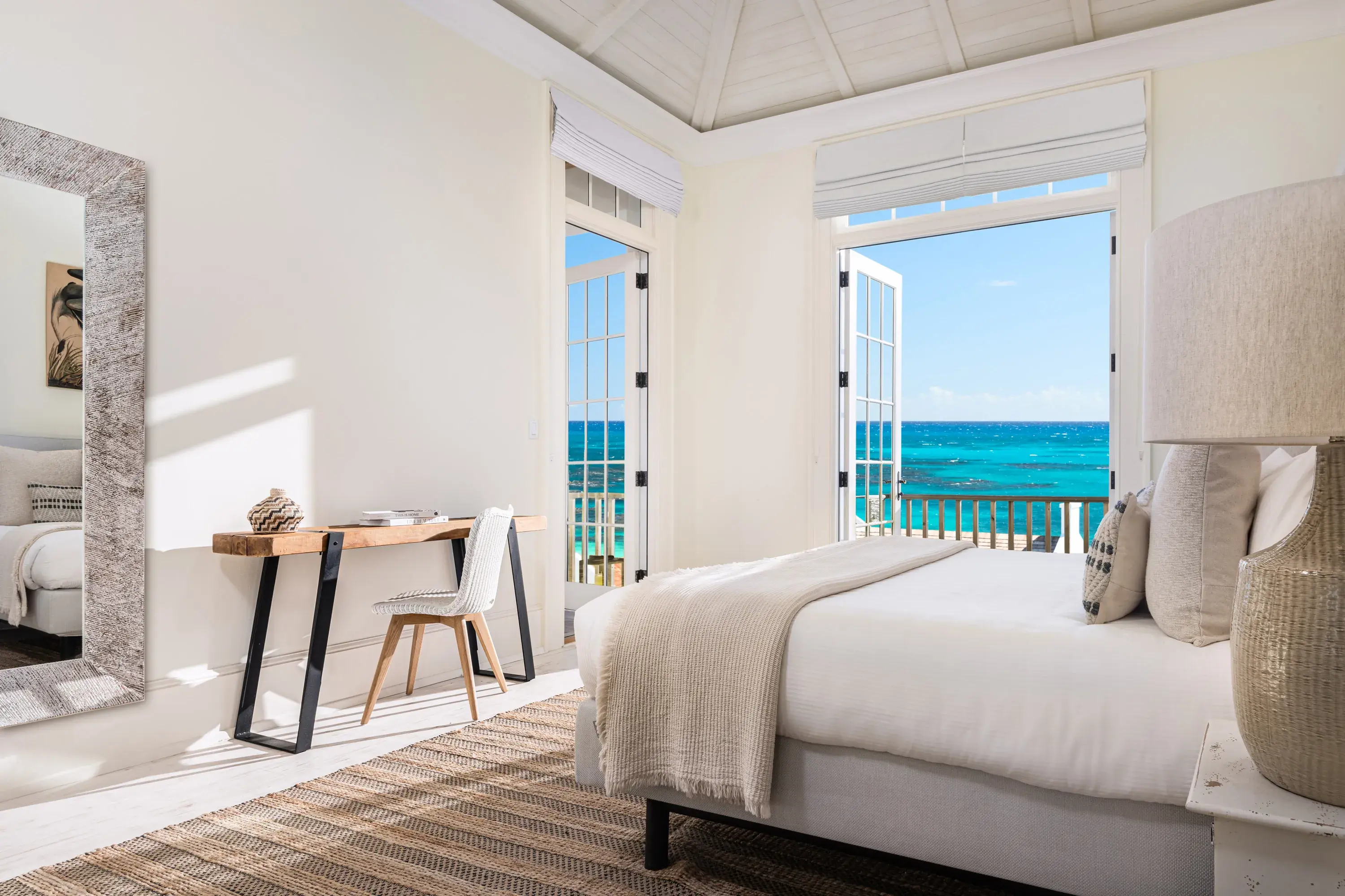 Neptune Villa master bedroom featuring relaxing natural decor, a comfy bed and two corner balcony doors overlooking the ocean