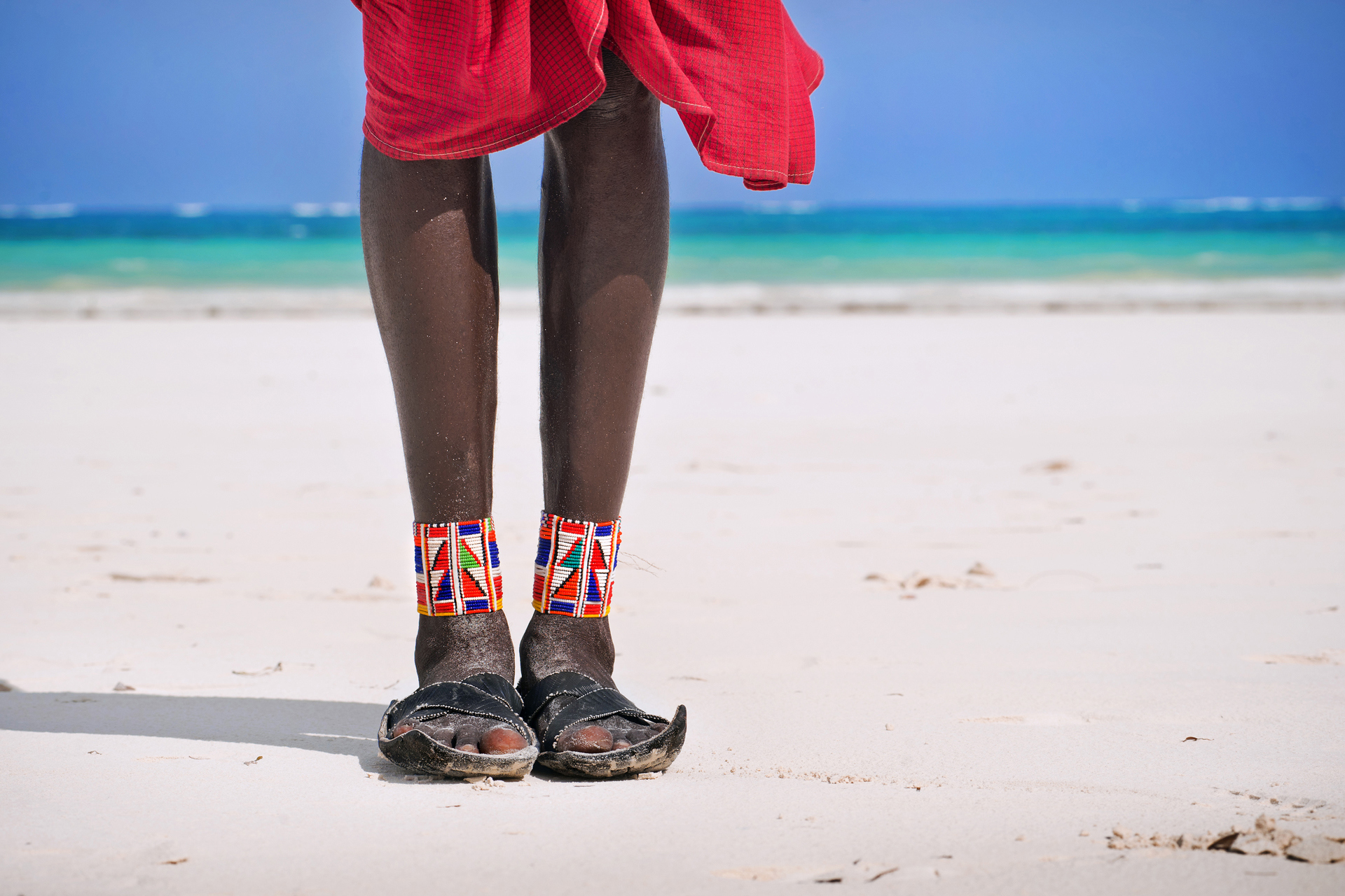 a person wearing sandals and red dress standing on a beach
