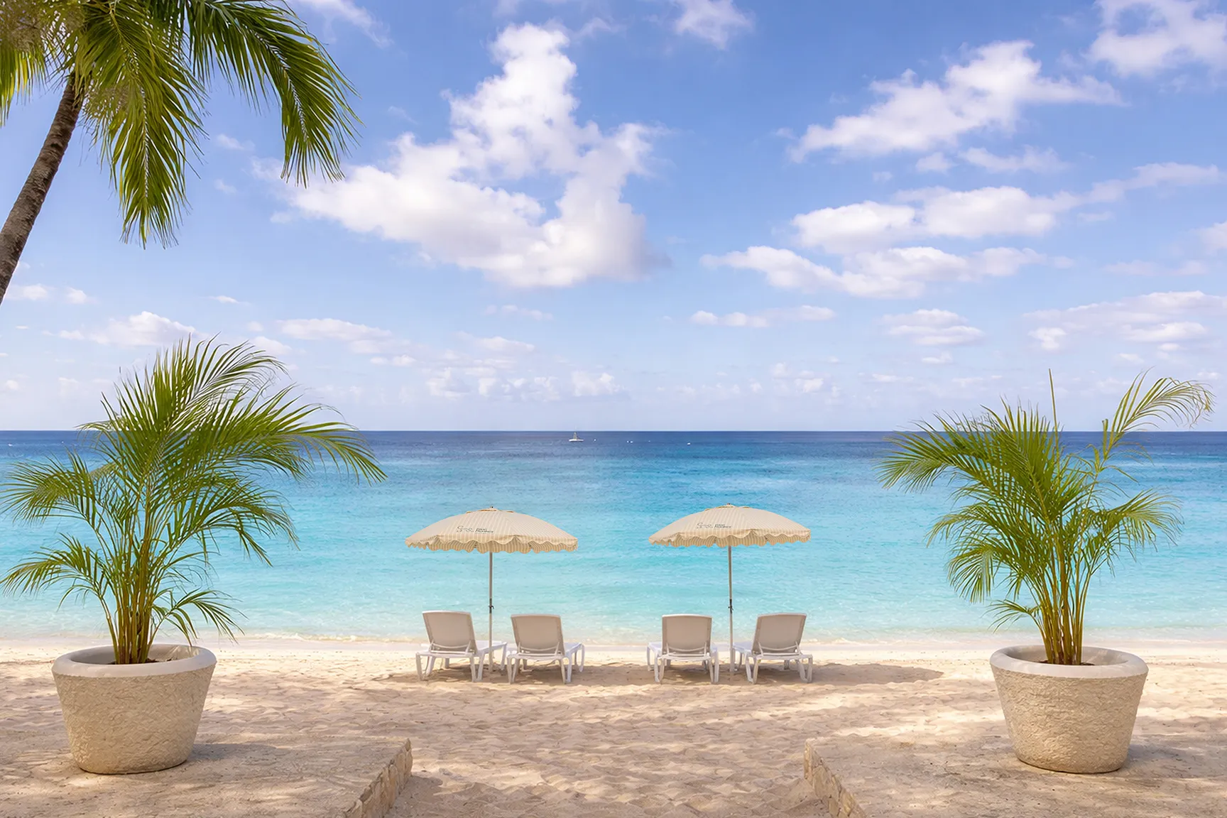 Sandy beach with lounge chairs and umbrellas overlooking turquoise ocean, framed by palm trees.