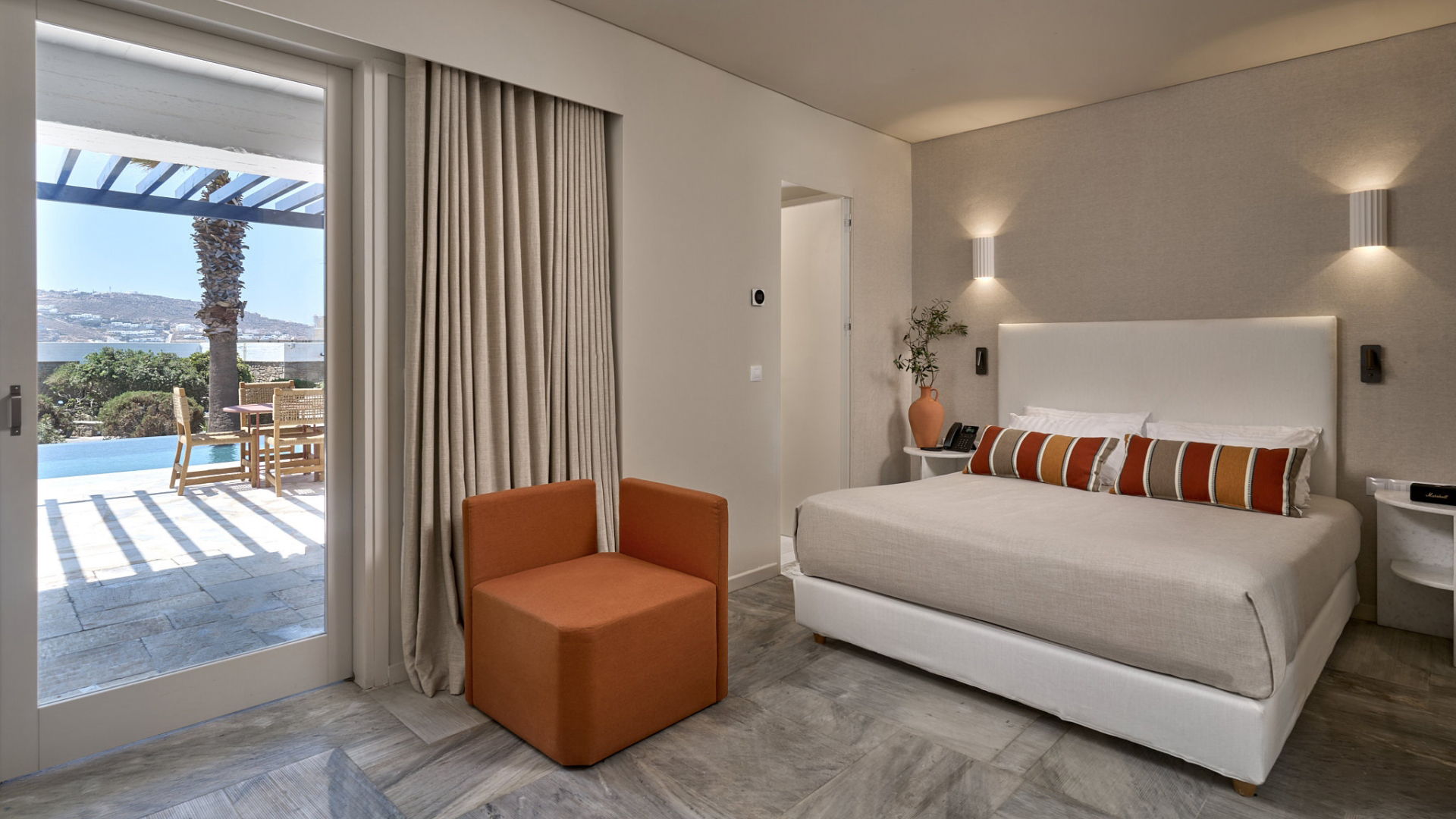 A modern suite in neutal tones with accents of red and orange and a view of the pool outside through the glass doors