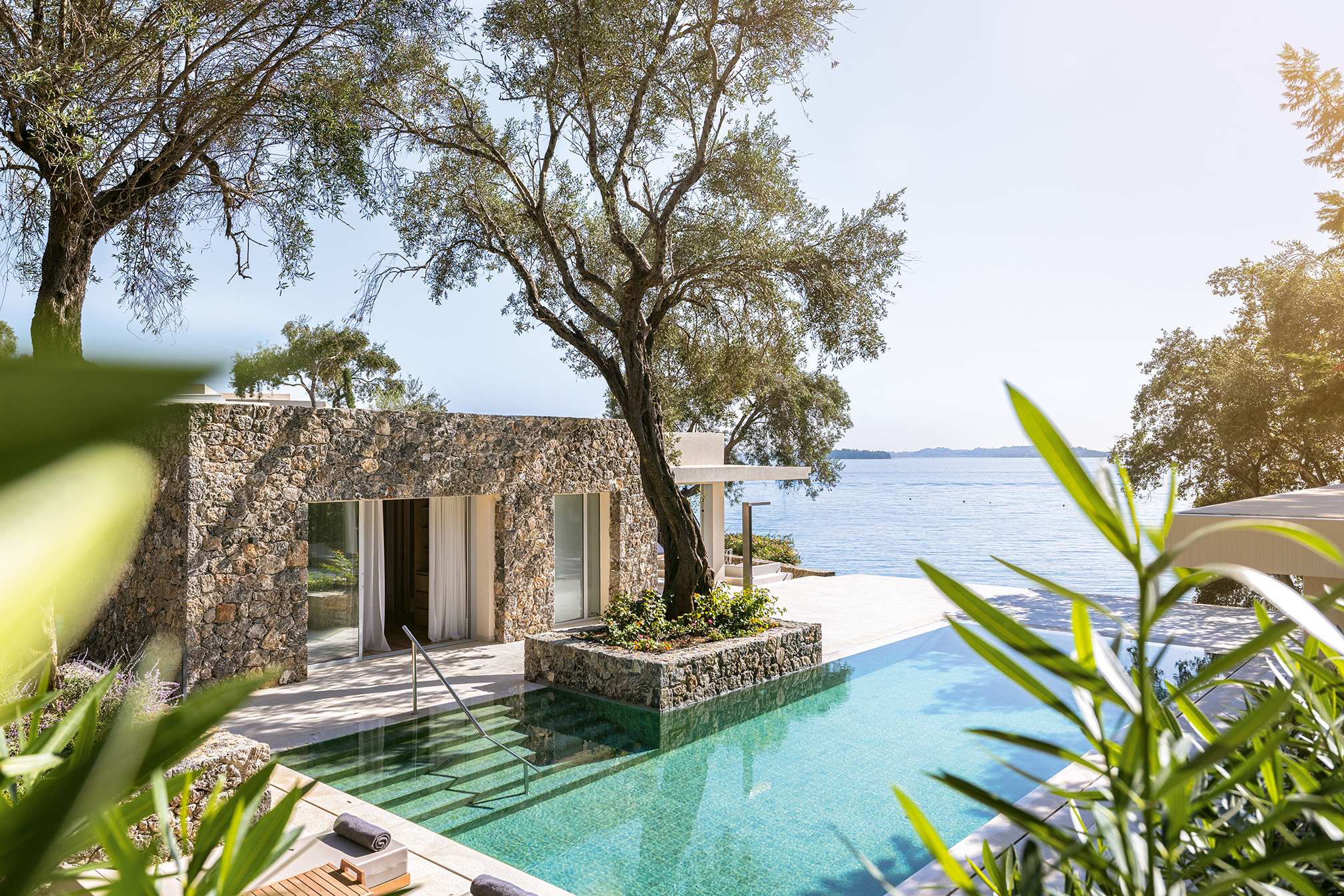 A stone villa at Grecotel Corfu Imperial and swimming pool surrounded by established trees with the sea behind