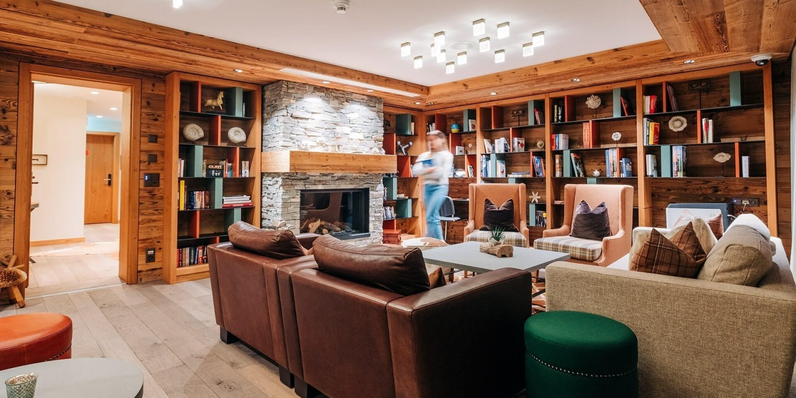 Cosy lounge with wooden interiors, leather seating, bookshelves, and a central stone fireplace.