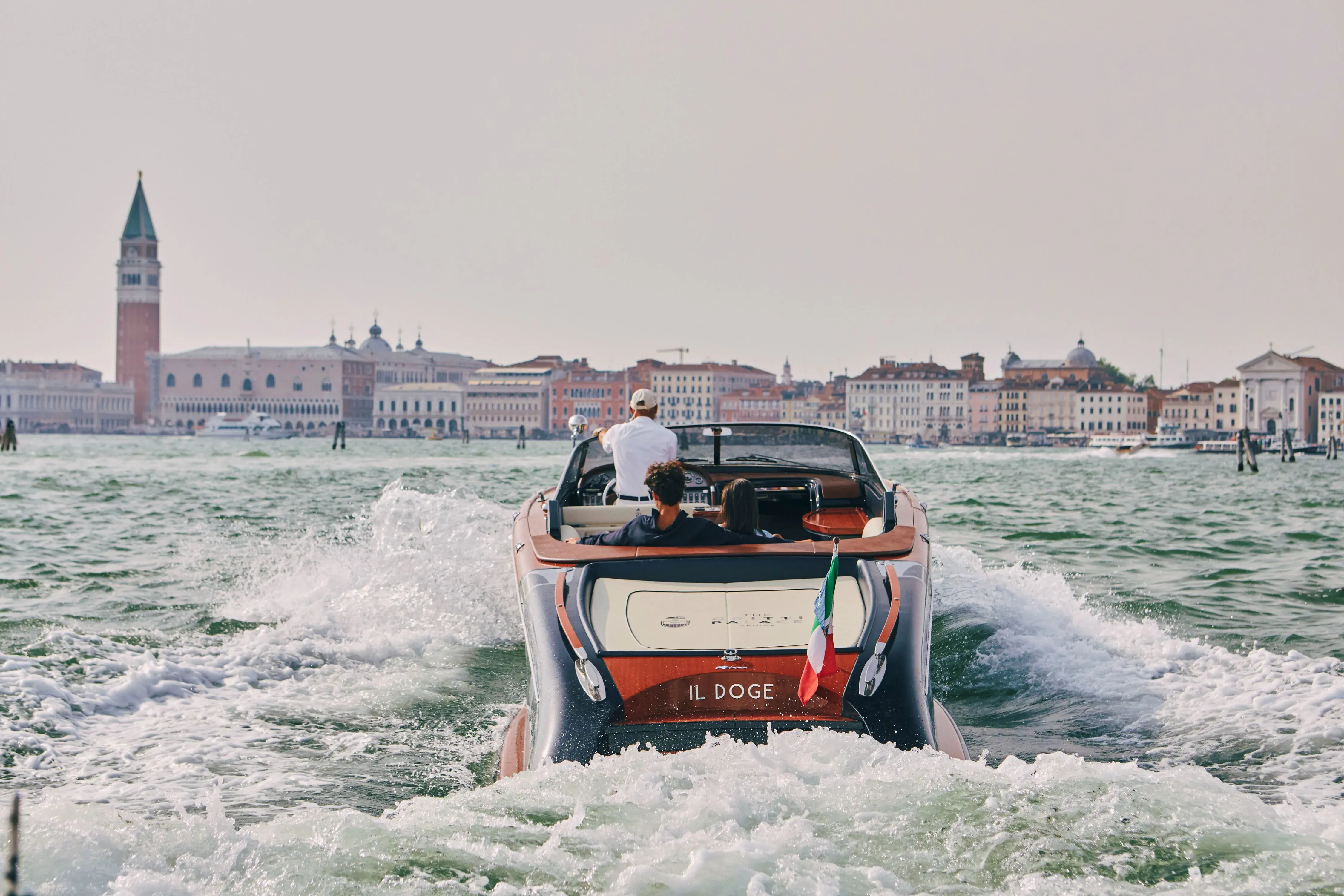 Luxury water taxi cruising towards Venice landmarks near The Gritti Palace with St. Mark’s Campanile in the background.