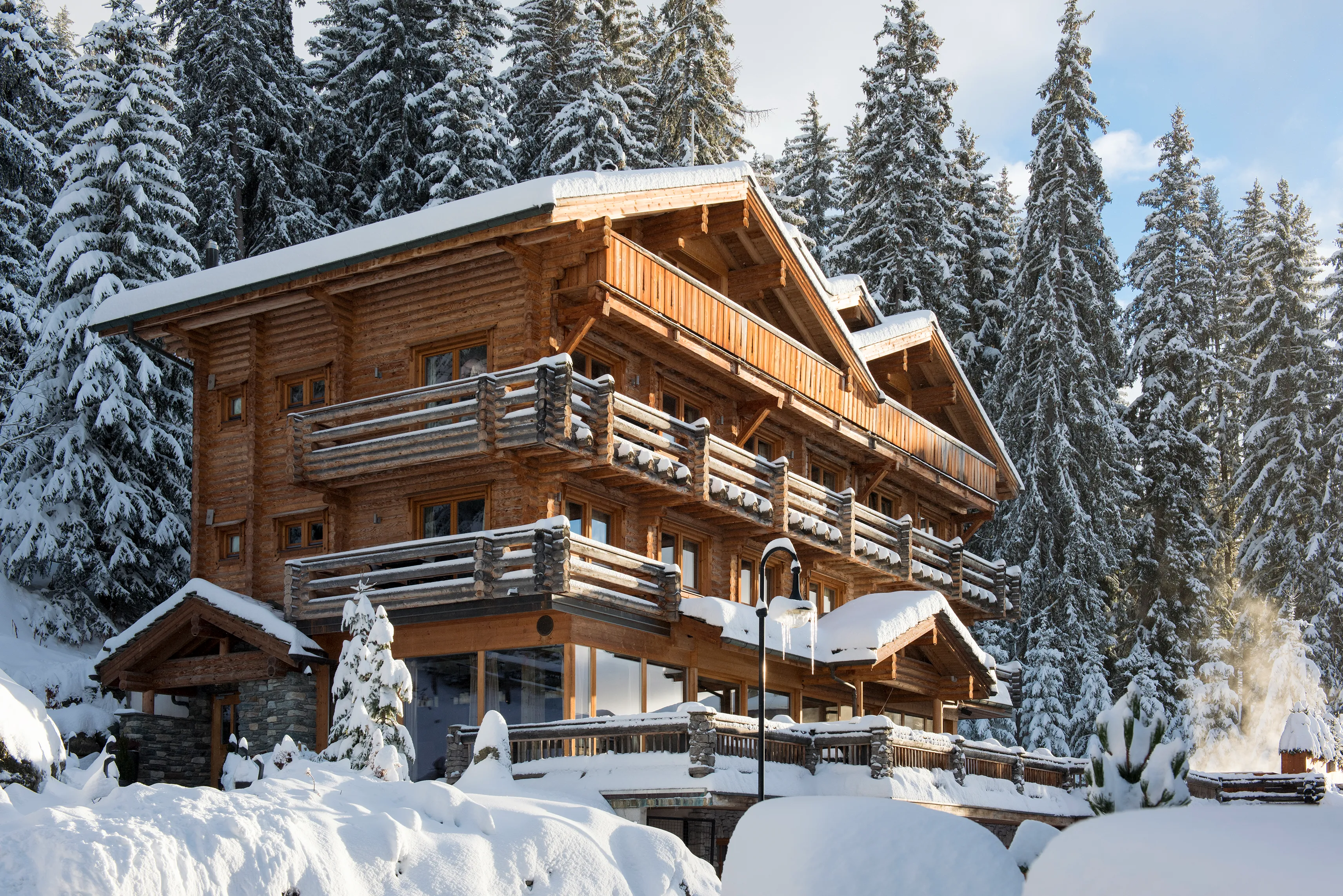 A large wooden chalet with wrap around balconies surrounded by snowy woodland 
