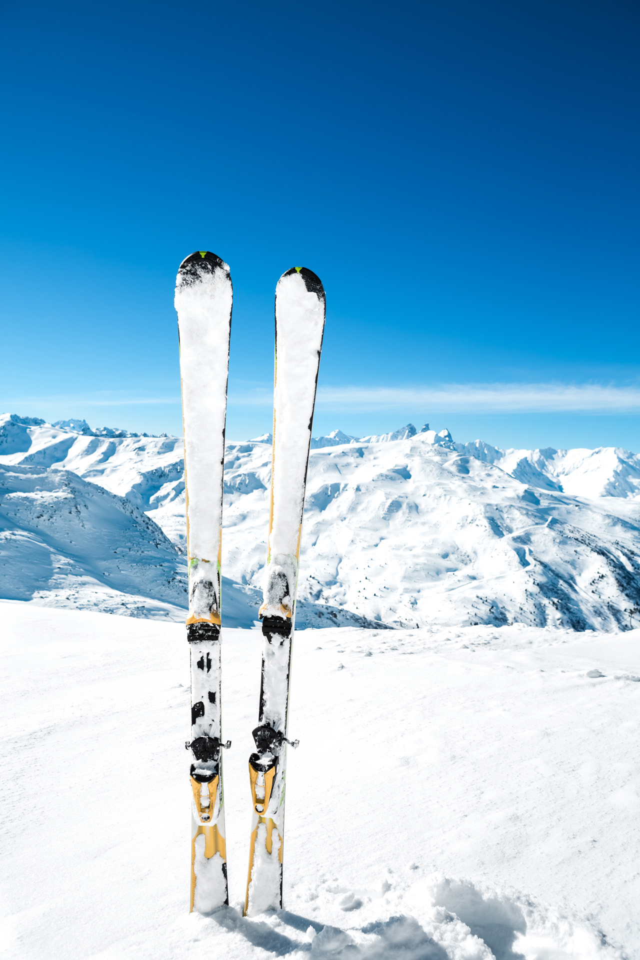 A pair of skiis sticking out of snow with mountains in the background