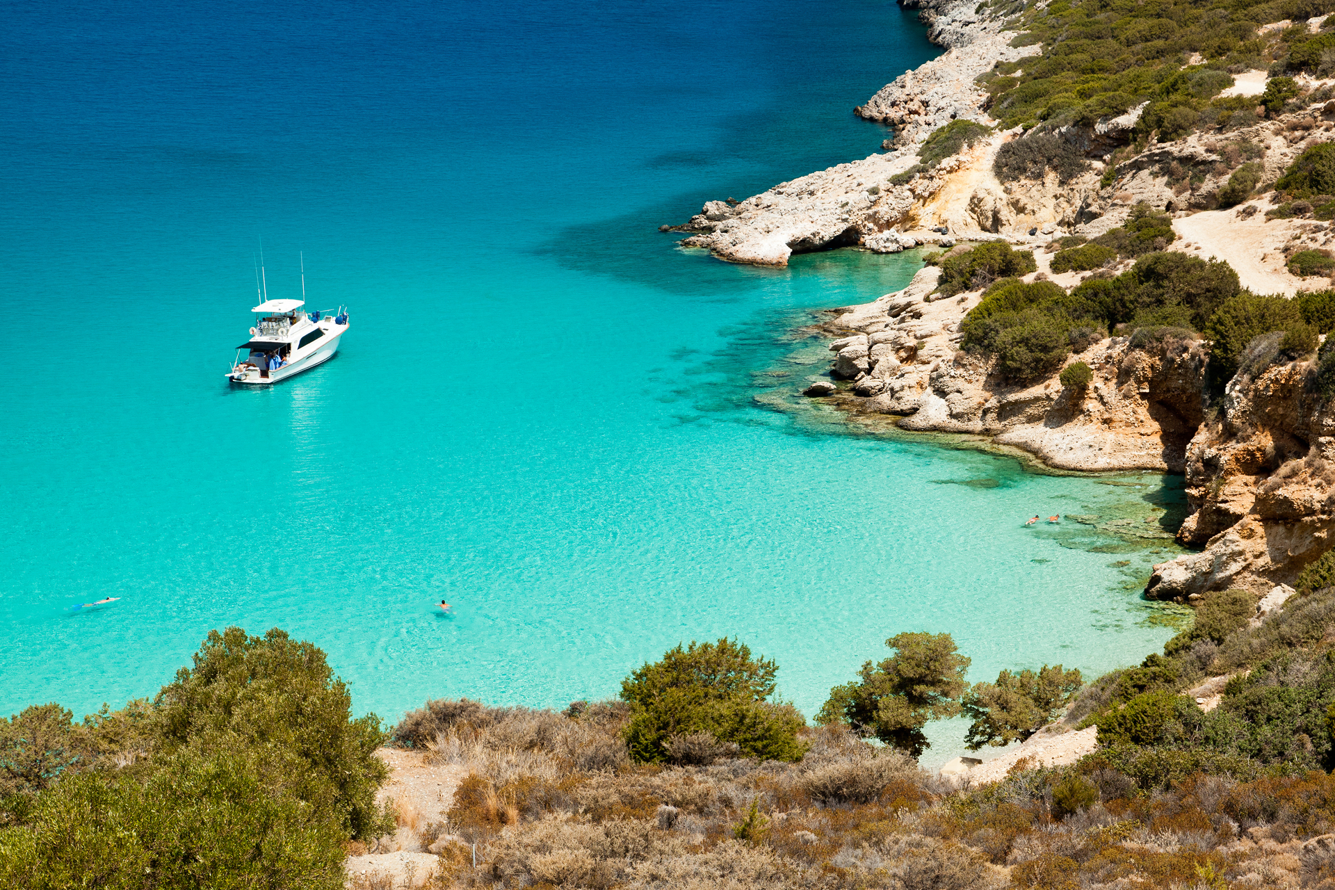A boat anchored in shallow clear water next to a rocky coastline