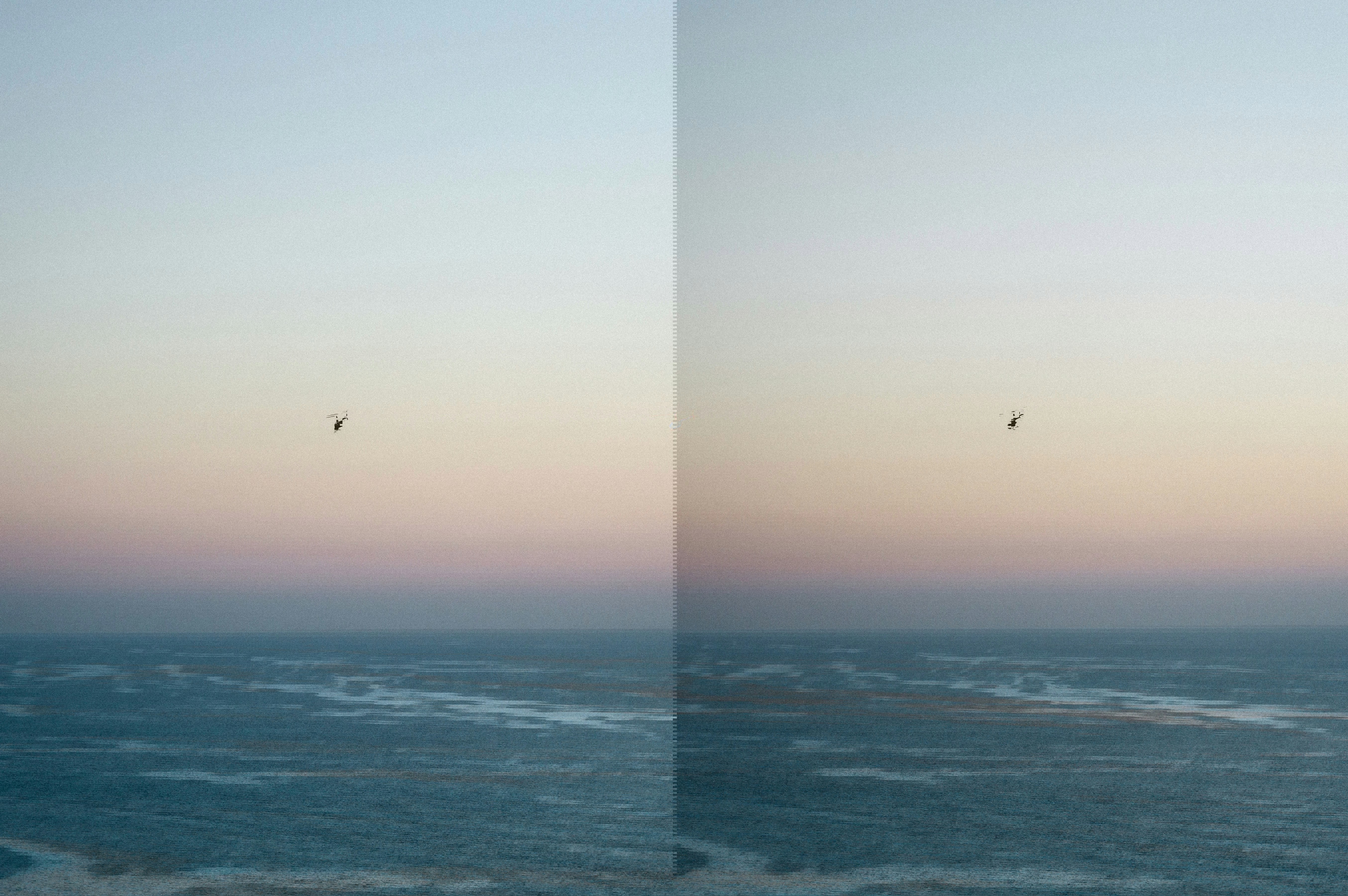Helicopter flying over a calm ocean at sunset with soft pastel colors across the sky.