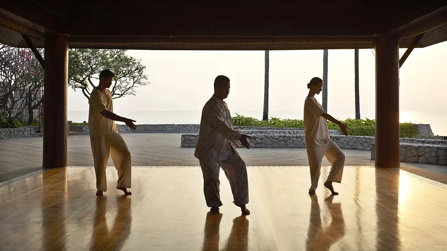 Guests practising tai chi at Chiva Som in an open pavilion overlooking the sea at sunrise.
