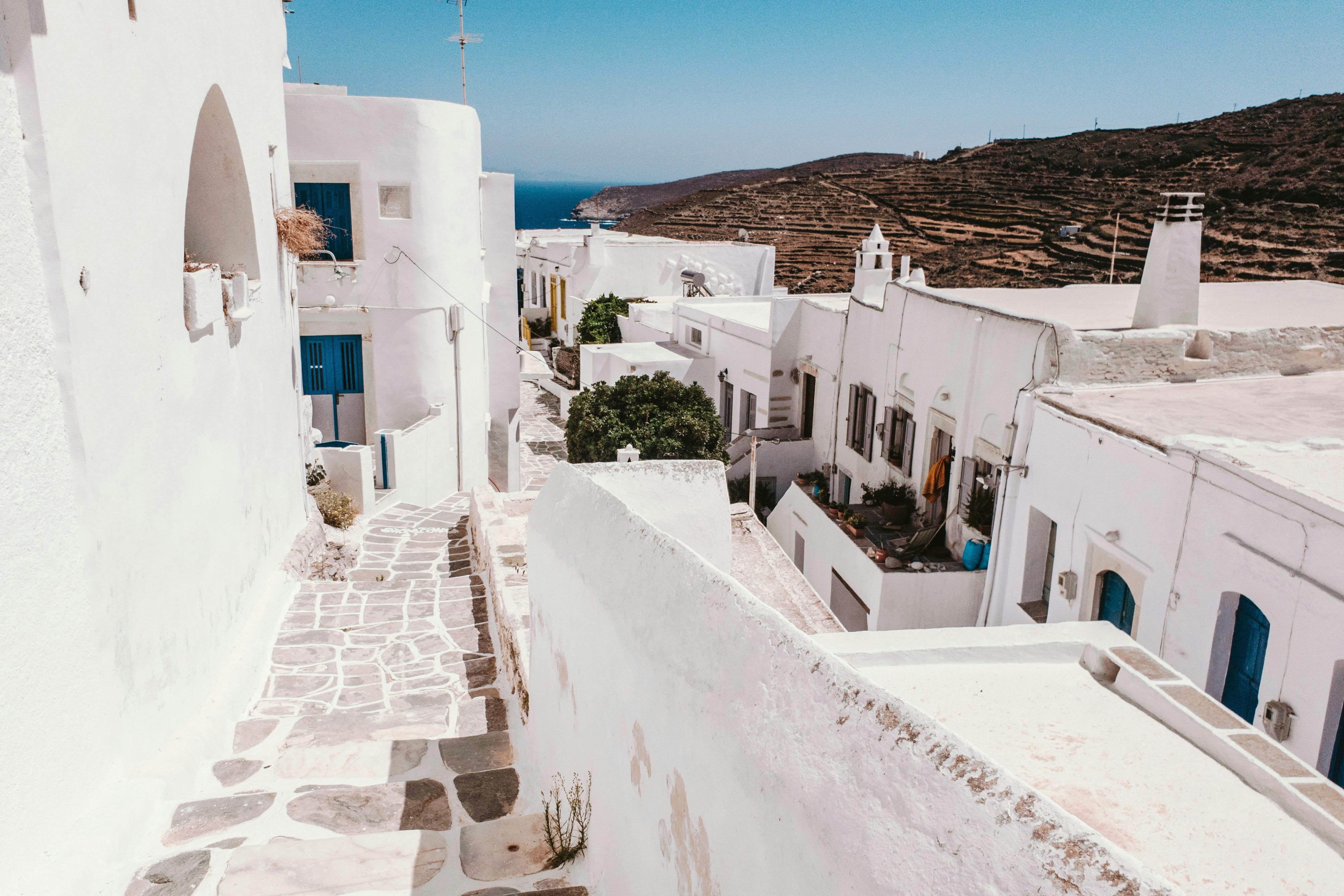 Cobbled street stretching down hill between whitewashed buildings on Sifnos with rugged hills in the background