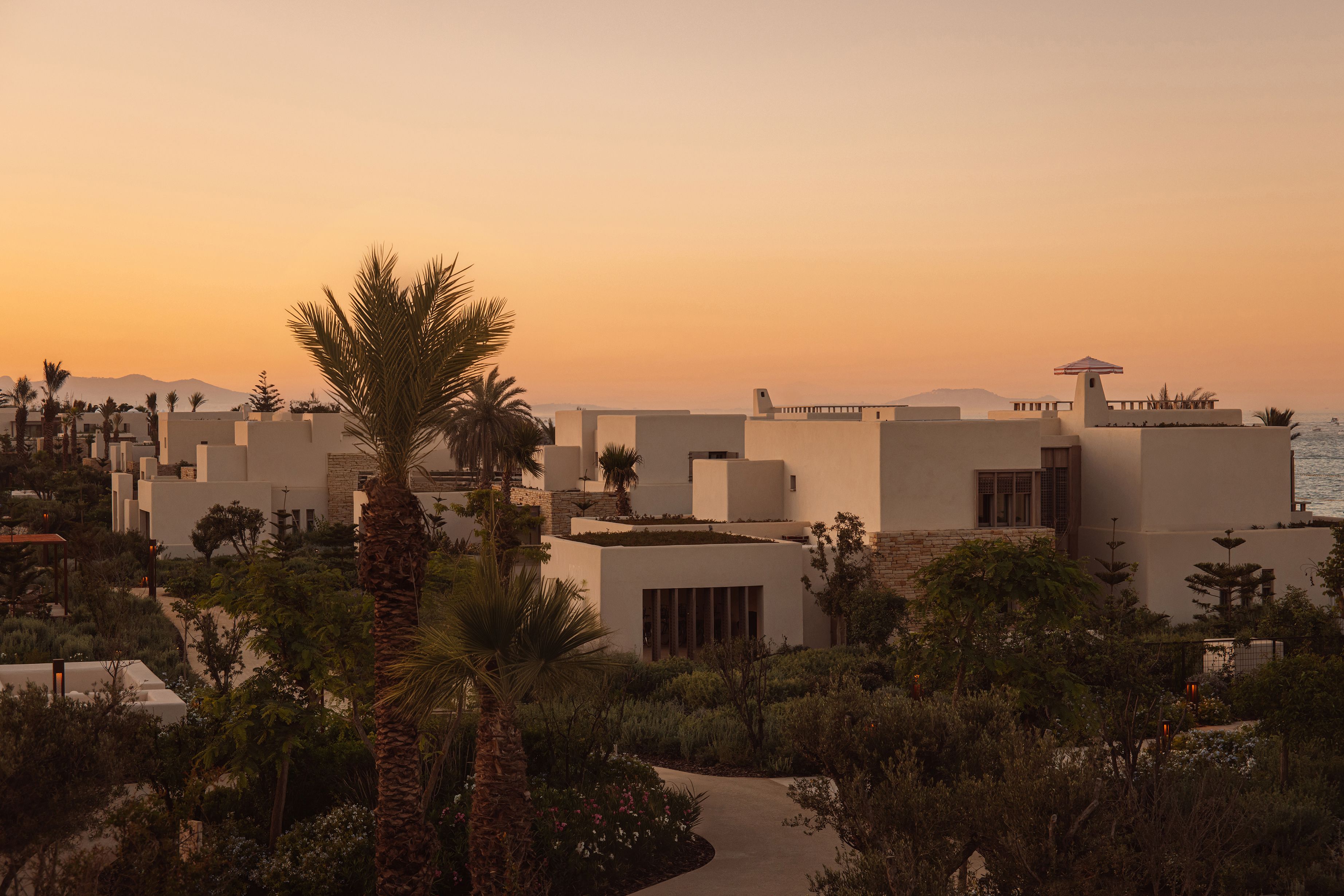 The pale exterior of Royal Mansour Tamuda Bay surrounded by trees at sunset