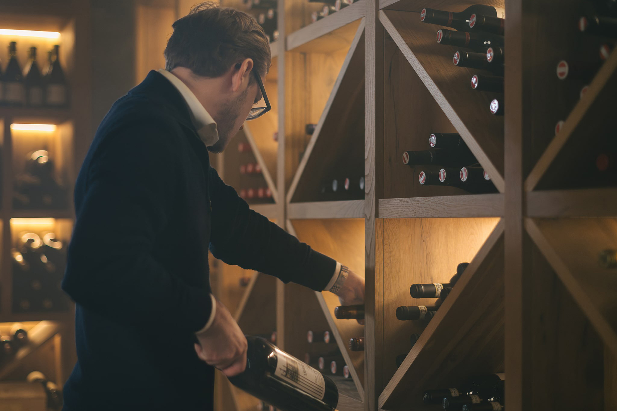 A sommelier choosing a bottle of wine from a wooden rack in a dimly lit cellar at a Gourmet and Wine Hotel Austria