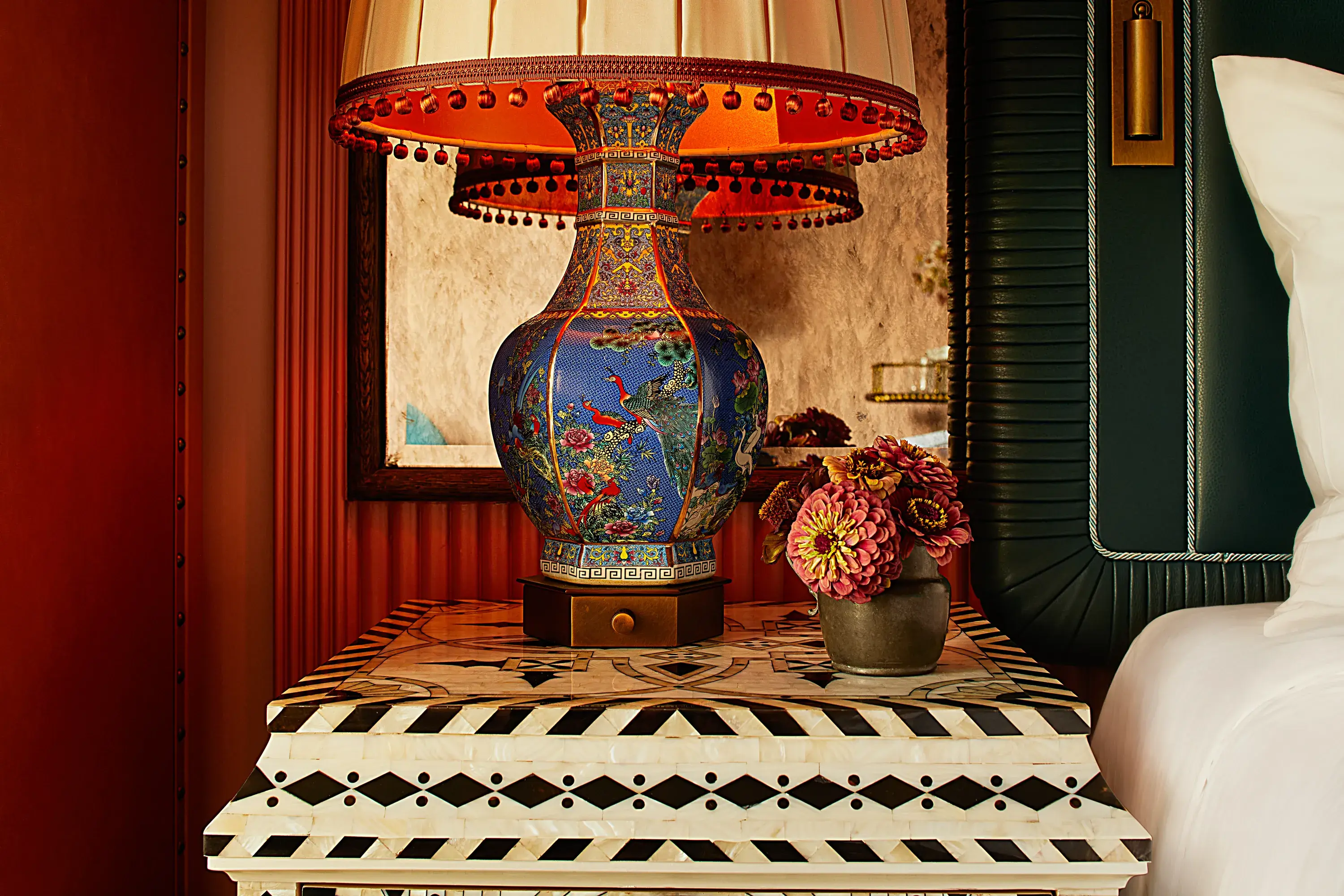 Colourful ceramic table lamp at Fifth Avenue Hotel with intricate floral patterns on a geometric black-and-white bedside table next to a small vase of pink flowers.