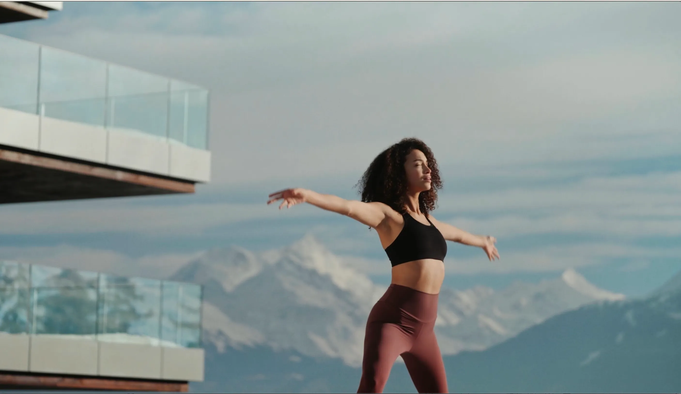 Woman practicing outdoor yoga as hotel balconies and alpine mountains are seen in the background