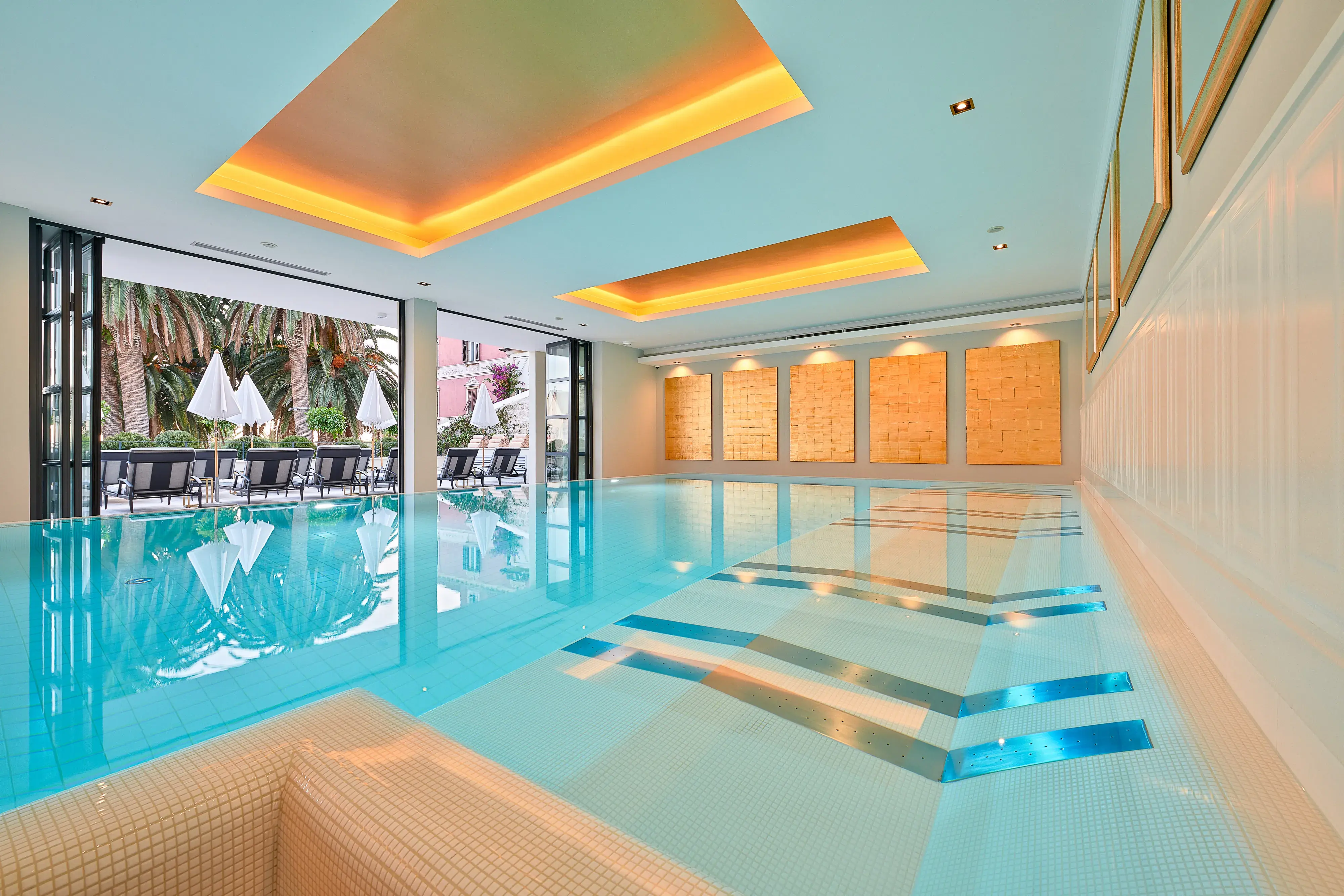 Indoor pool at Palace Elisabeth in Croatia set beneath warm ceiling lights and featuring in-pool loungers with a glimpse of a sun deck outside