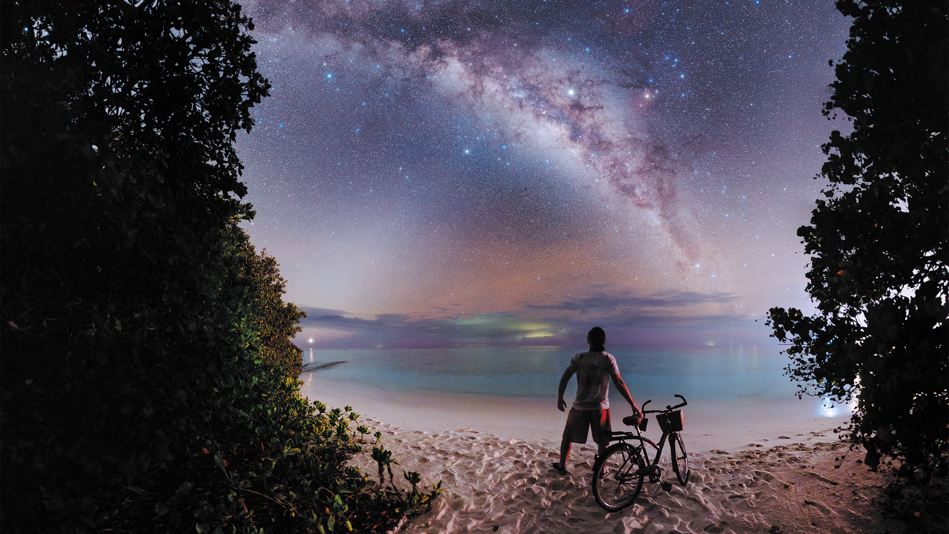 A man on a beach looking up at the starry night sky over Soneva Fushi