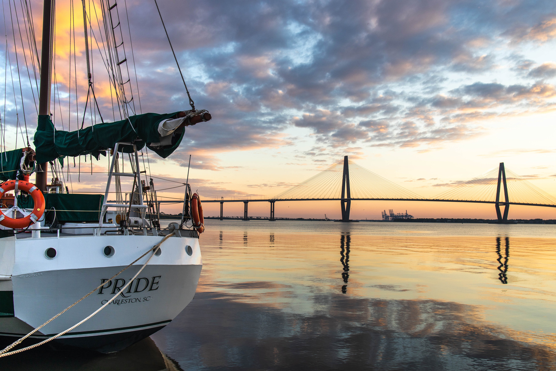 A sailboat docked at a dock with the long Ravenel Bridge in Charleston