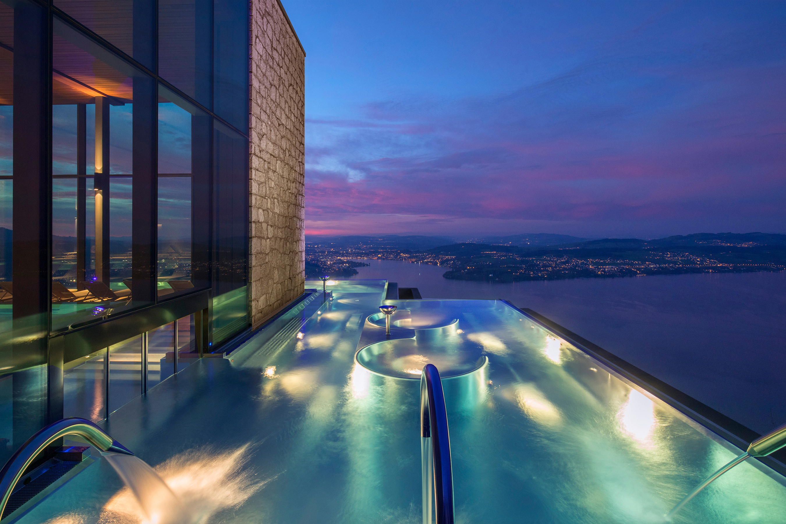 An outdoor infinity spa pool lit up at night with a sweeping view of the surrounding landscape