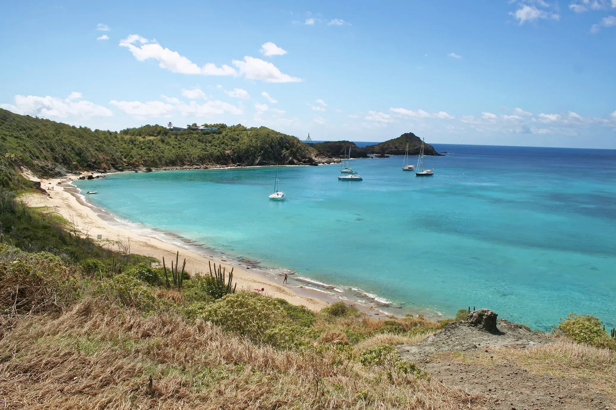 Scenic turquoise bay at Colombier Beach with sailboats anchored near a quiet sandy beach surrounded by green coastal hills.