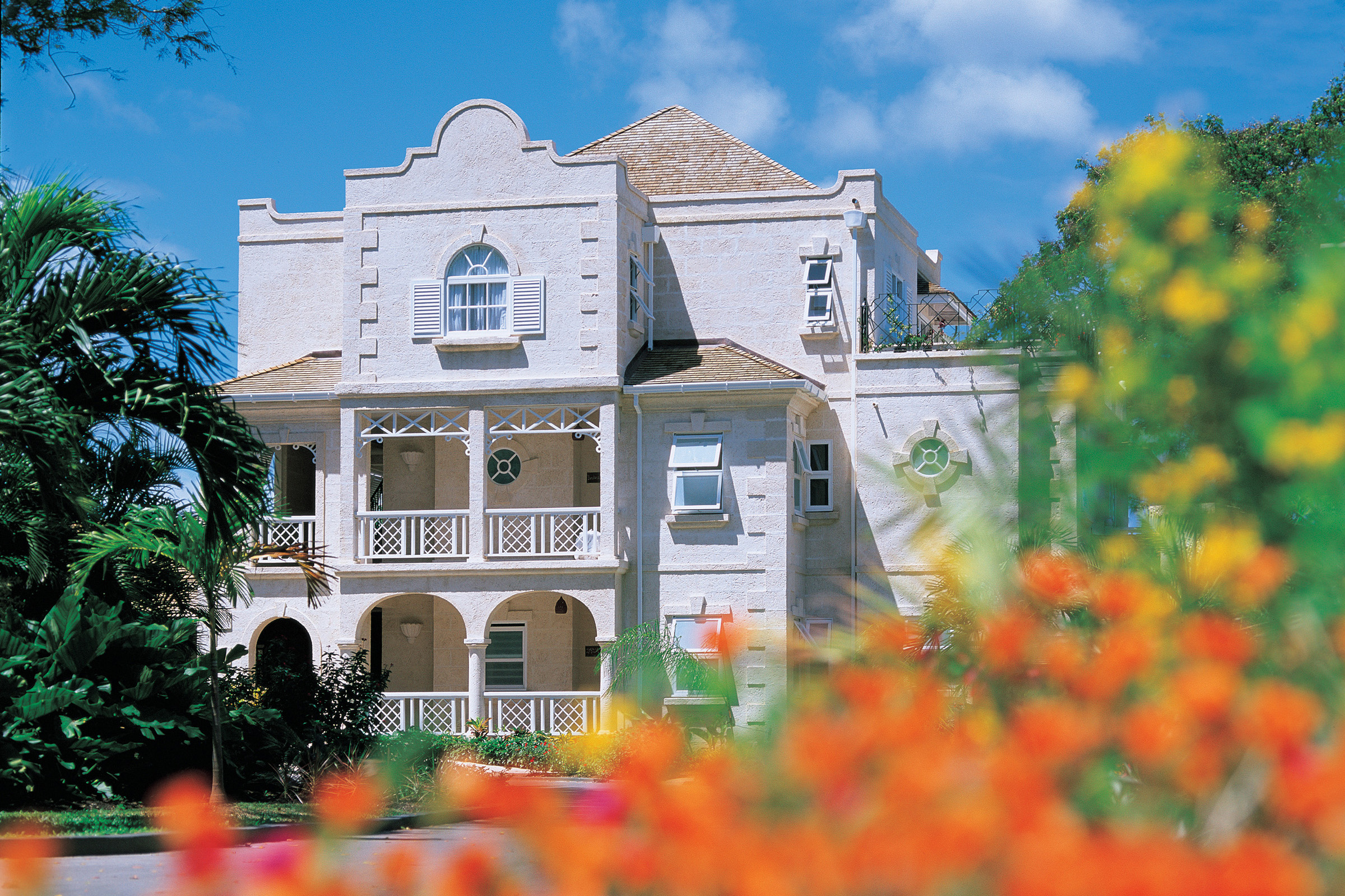 The large white facade of Coral Reef Club with balconies sitting among orange flowers