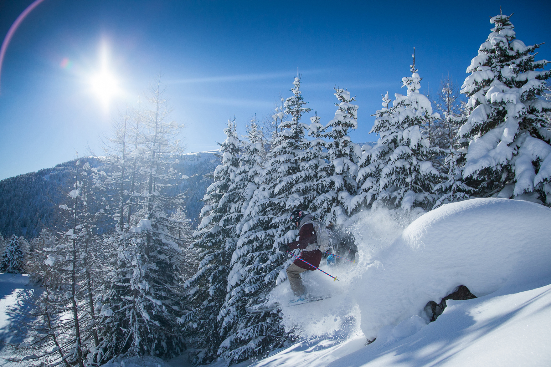 Skier jumping downhill with sun and trees in background in Italy