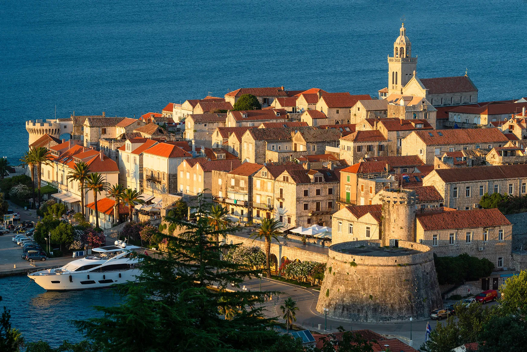 Historic coastal town with stone buildings, church tower, and waterfront marina.