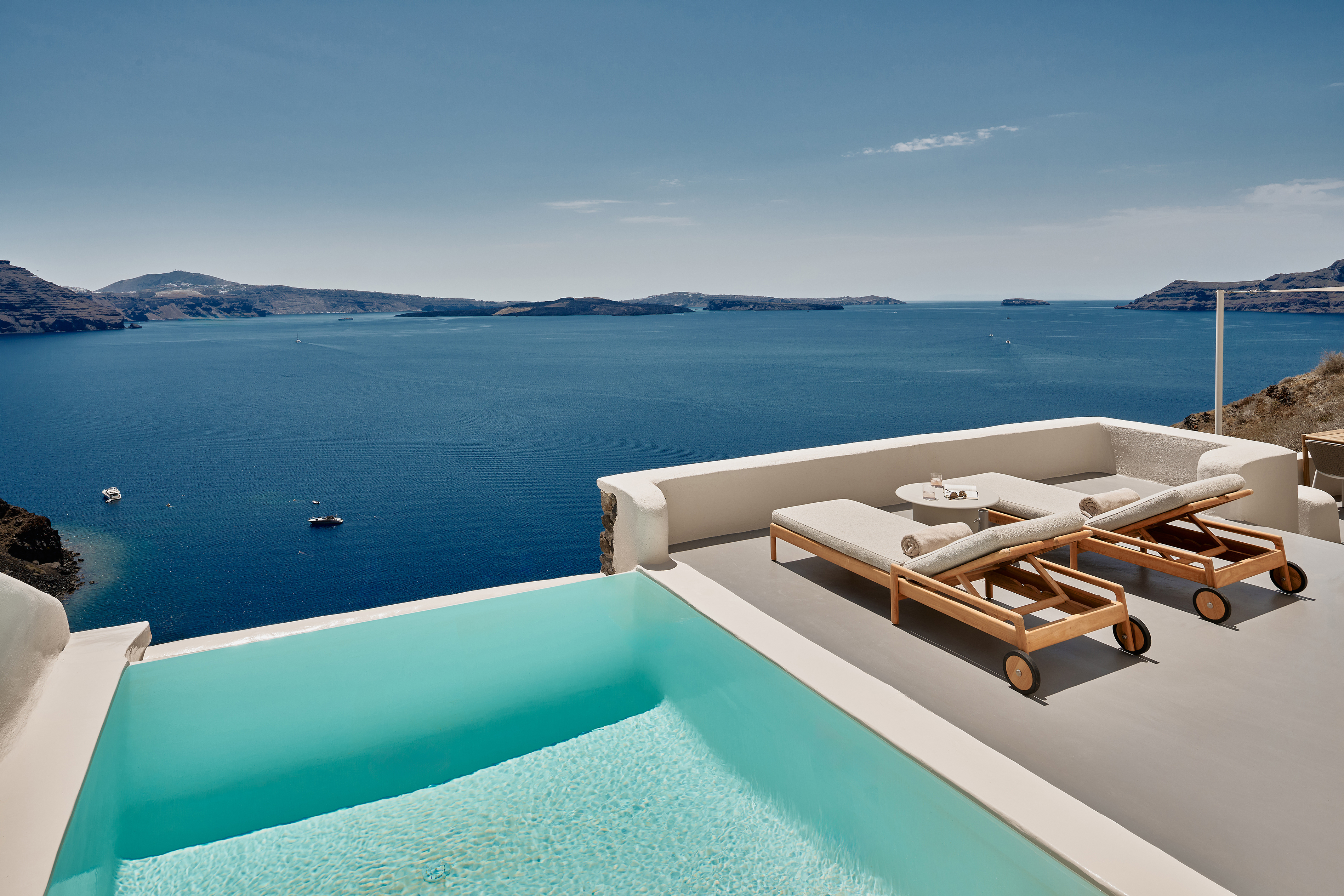 The terrace of a villa at Mystique hotel in Santorini with a private pool and sun loungers overlooking the sweeping ocean landscape