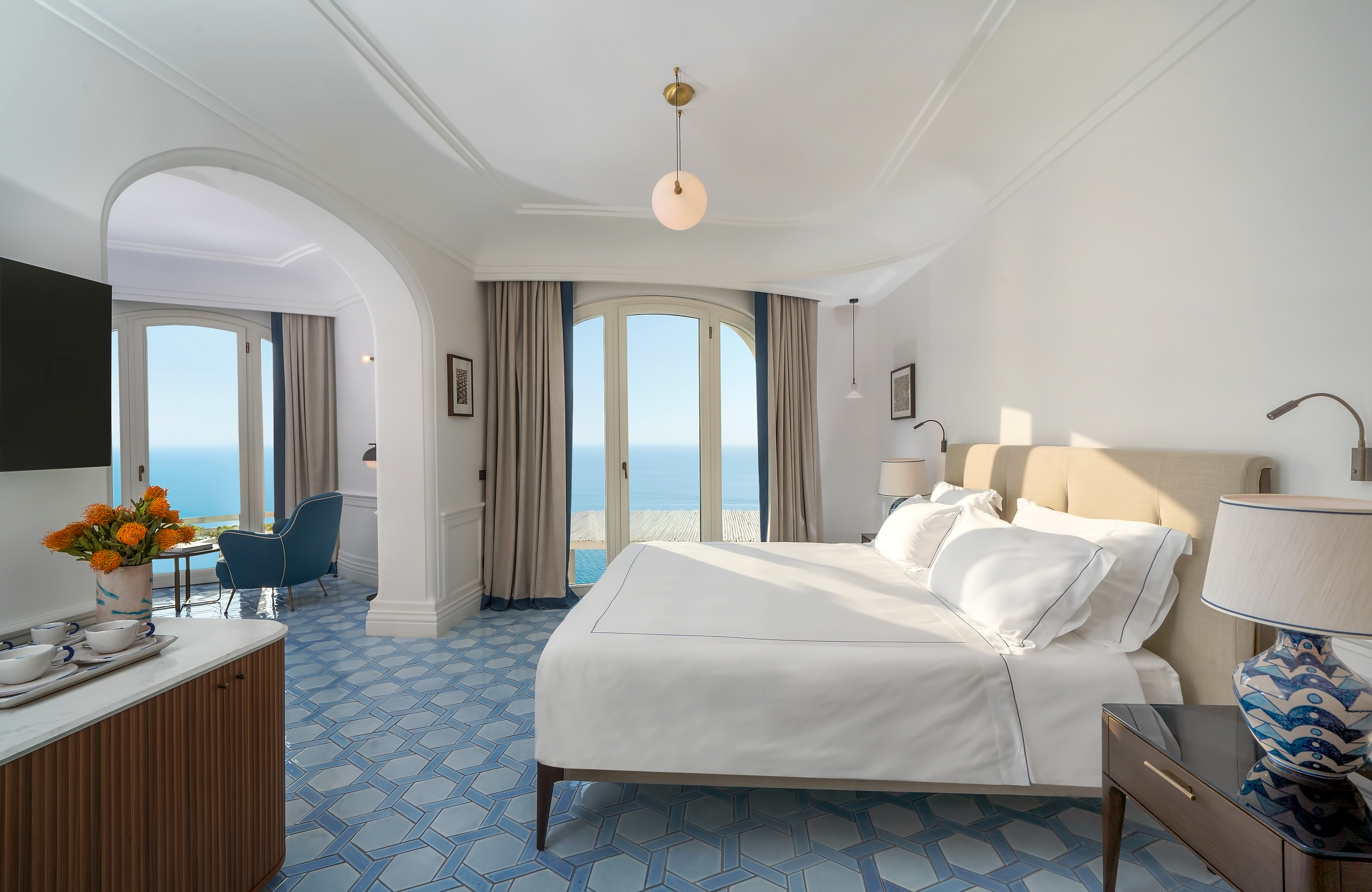 Luxurious junior suite at Borgo Santandrea in Amalfi with elegant decor, king-sized bed, and panoramic sea views through large windows.