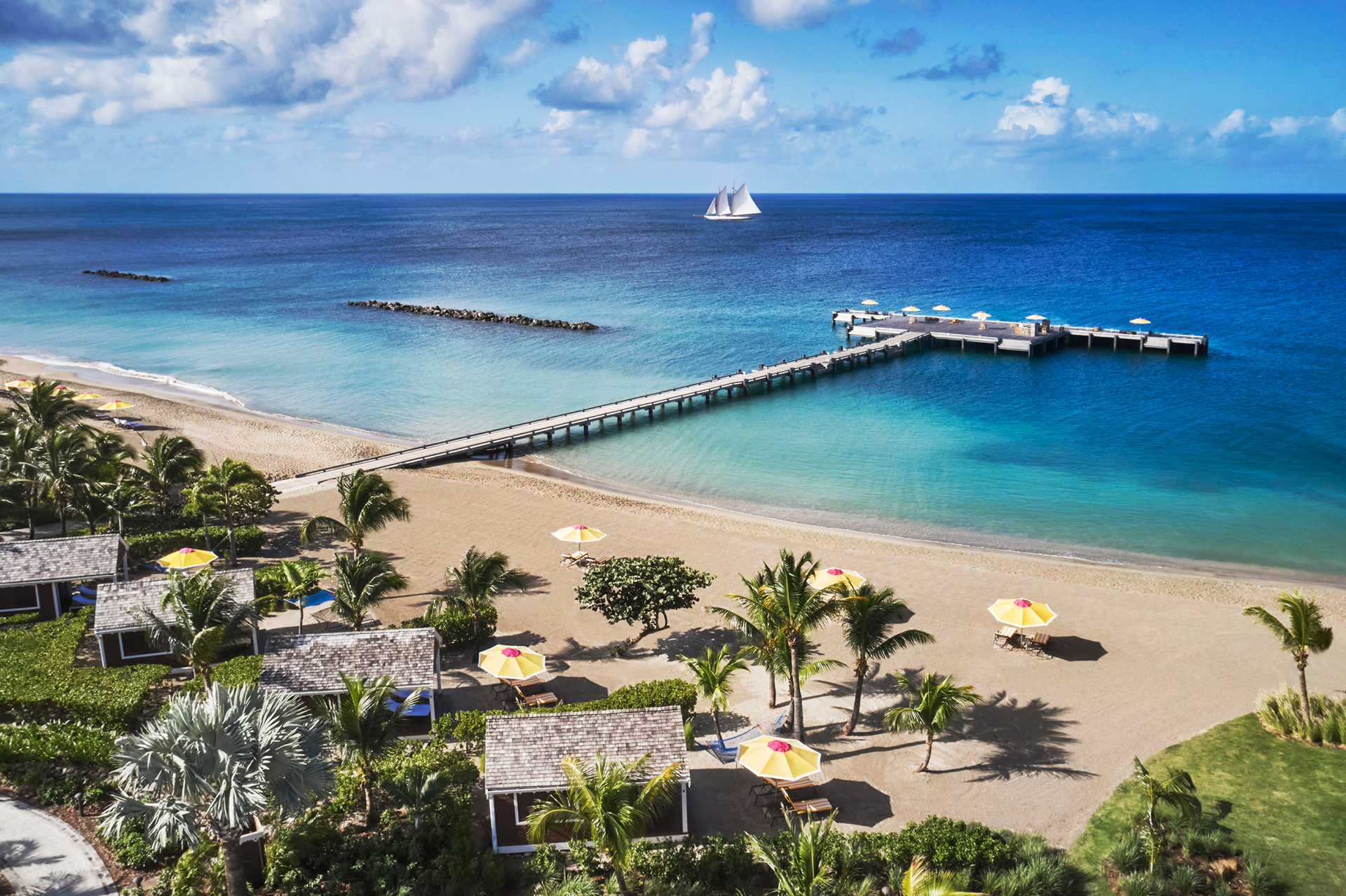 Sun loungers and umbrellas situated on the Four Seasons Resort Nevis beach along with an outstretching pier