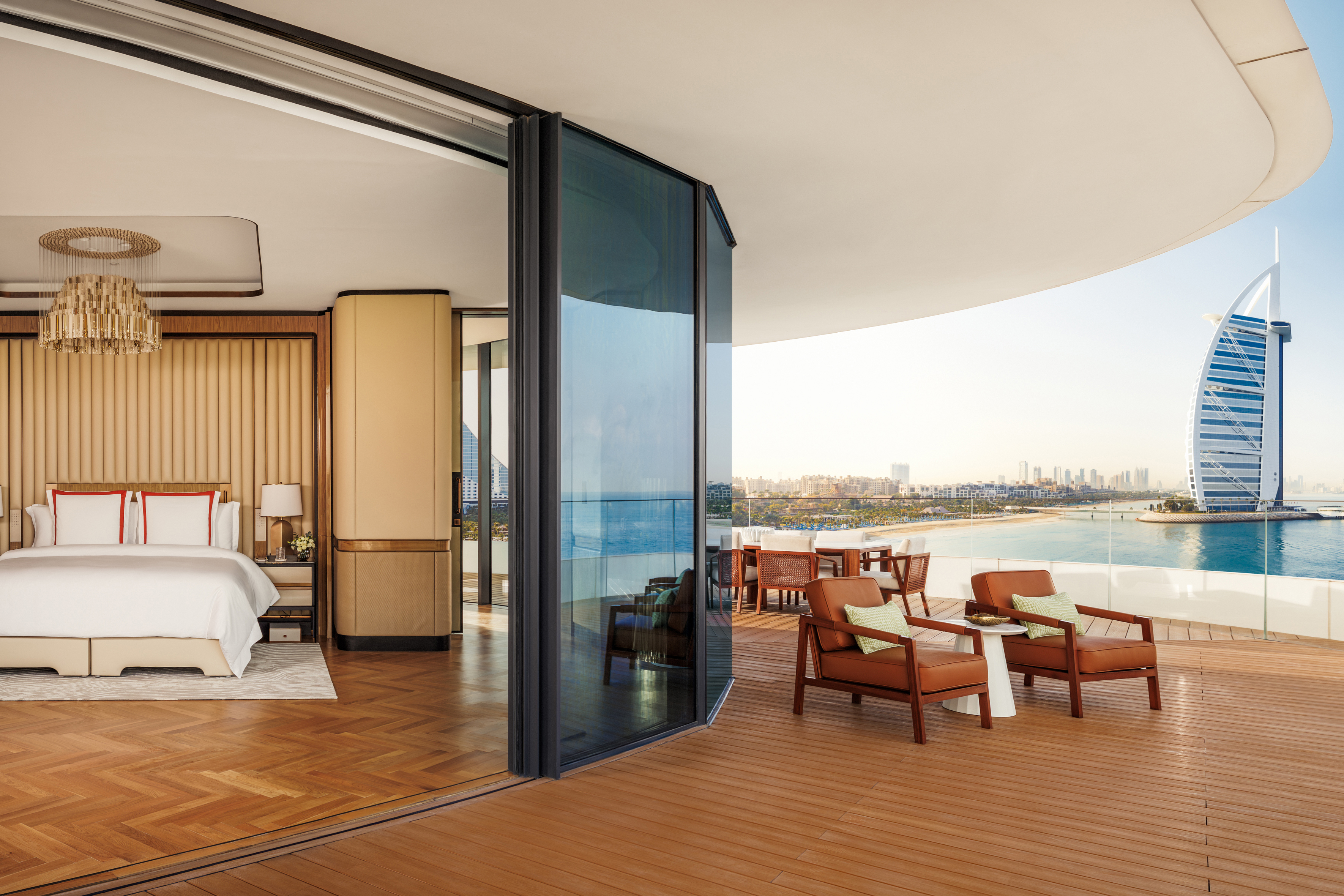 The terrace of a large suite at Jumeriah Marsa Al Arab featuring wooden furniture and a glimpse of the bedroom with the Burj Al Arab in the background