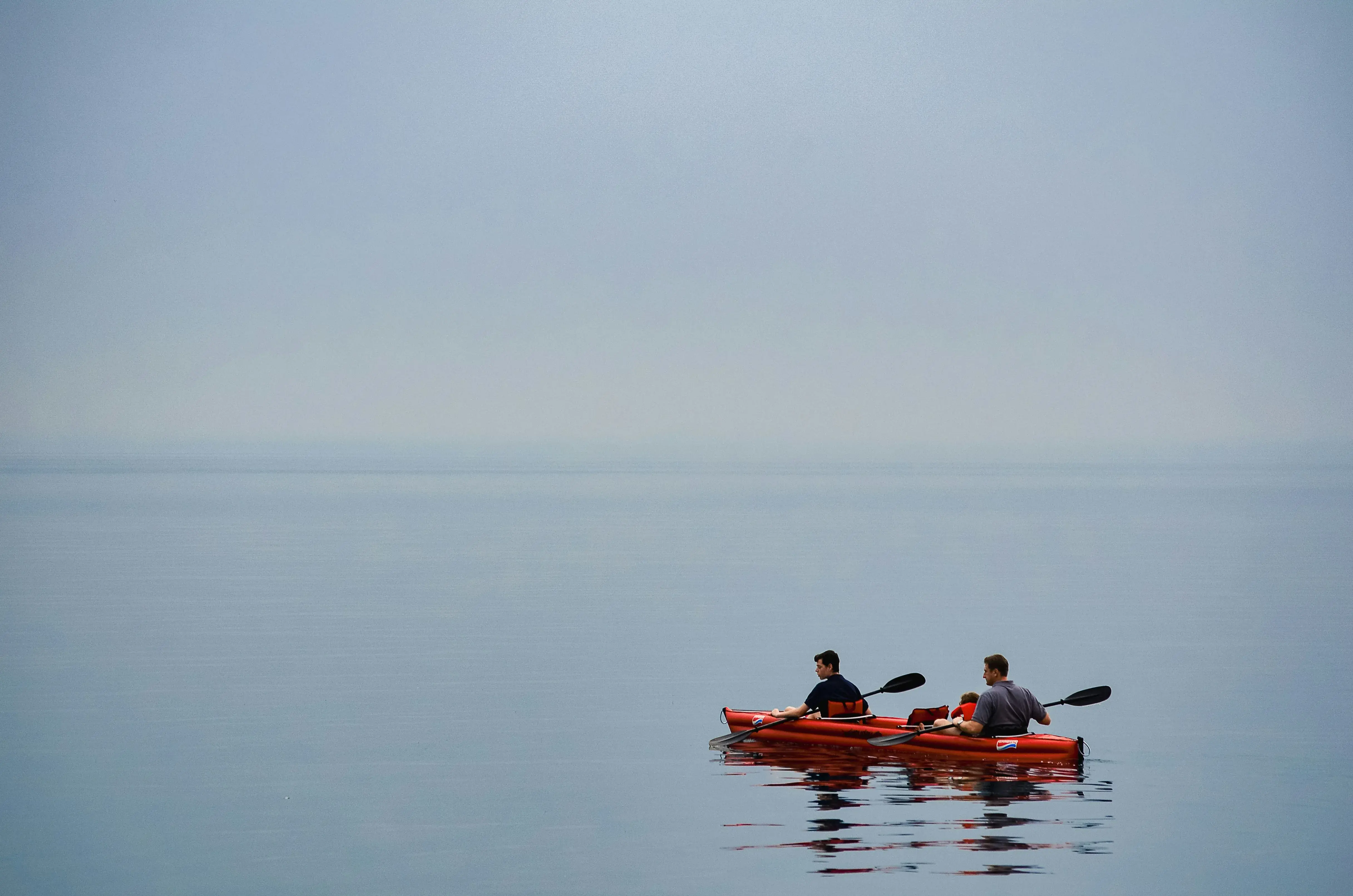 Two people kayaking on calm water under a clear, misty sky.