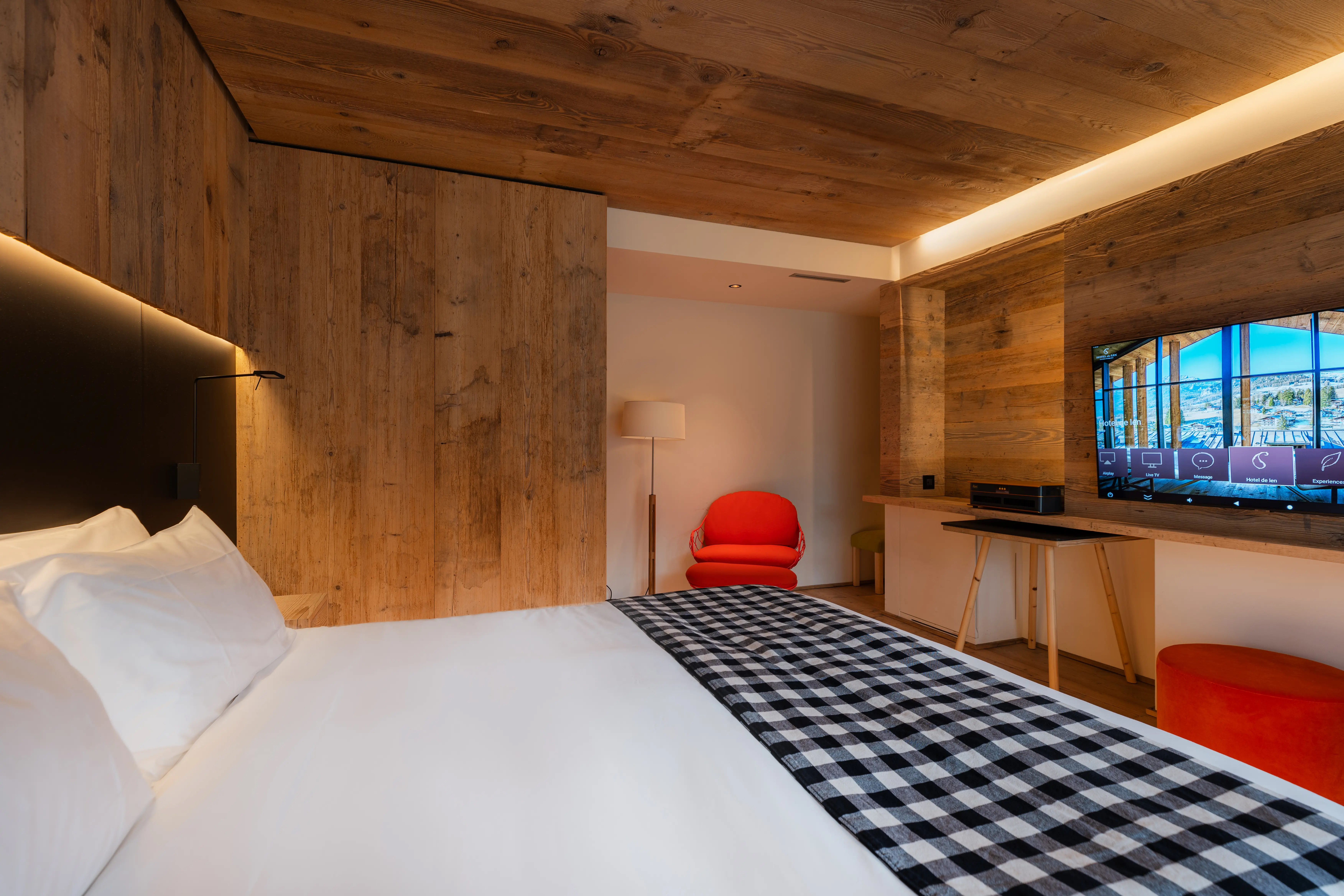 Hotel de Len deluxe room with wooden ceilings featuring a bed with a checkered throw, red furniture and television 