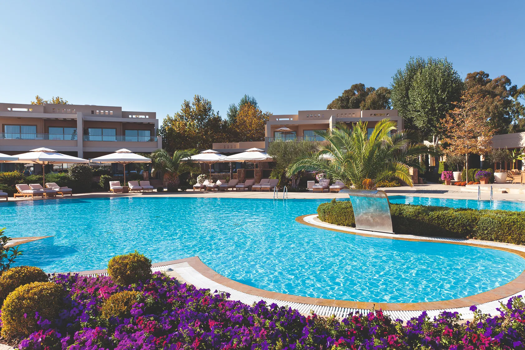 Luxurious pool area at Sani Asterias in Halkidiki featuring crystal‑blue water, landscaped gardens and elegant suites under clear Mediterranean skies.