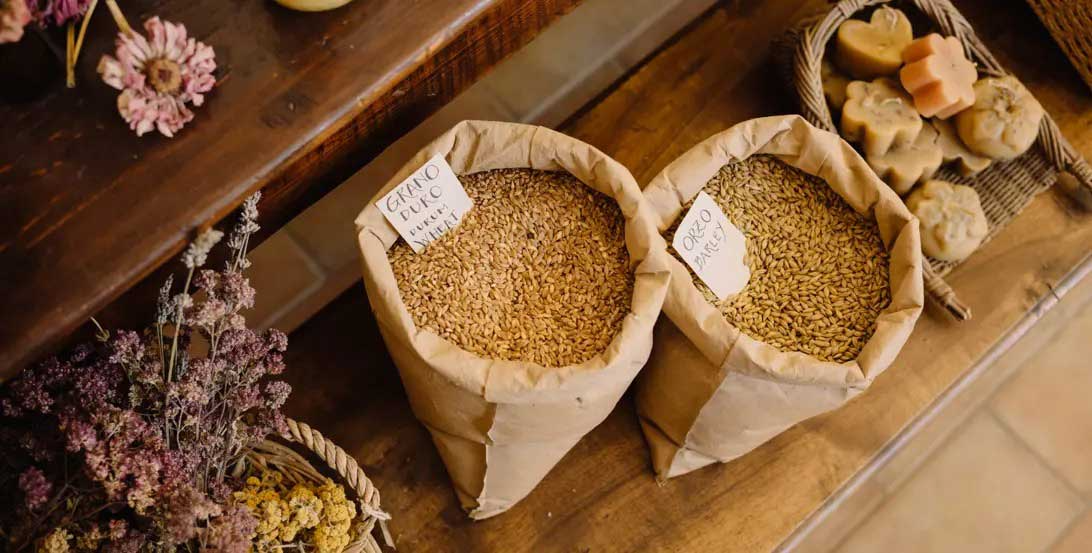 Paper bags filled with grains displayed alongside dried flowers and handmade soaps on a wooden table.