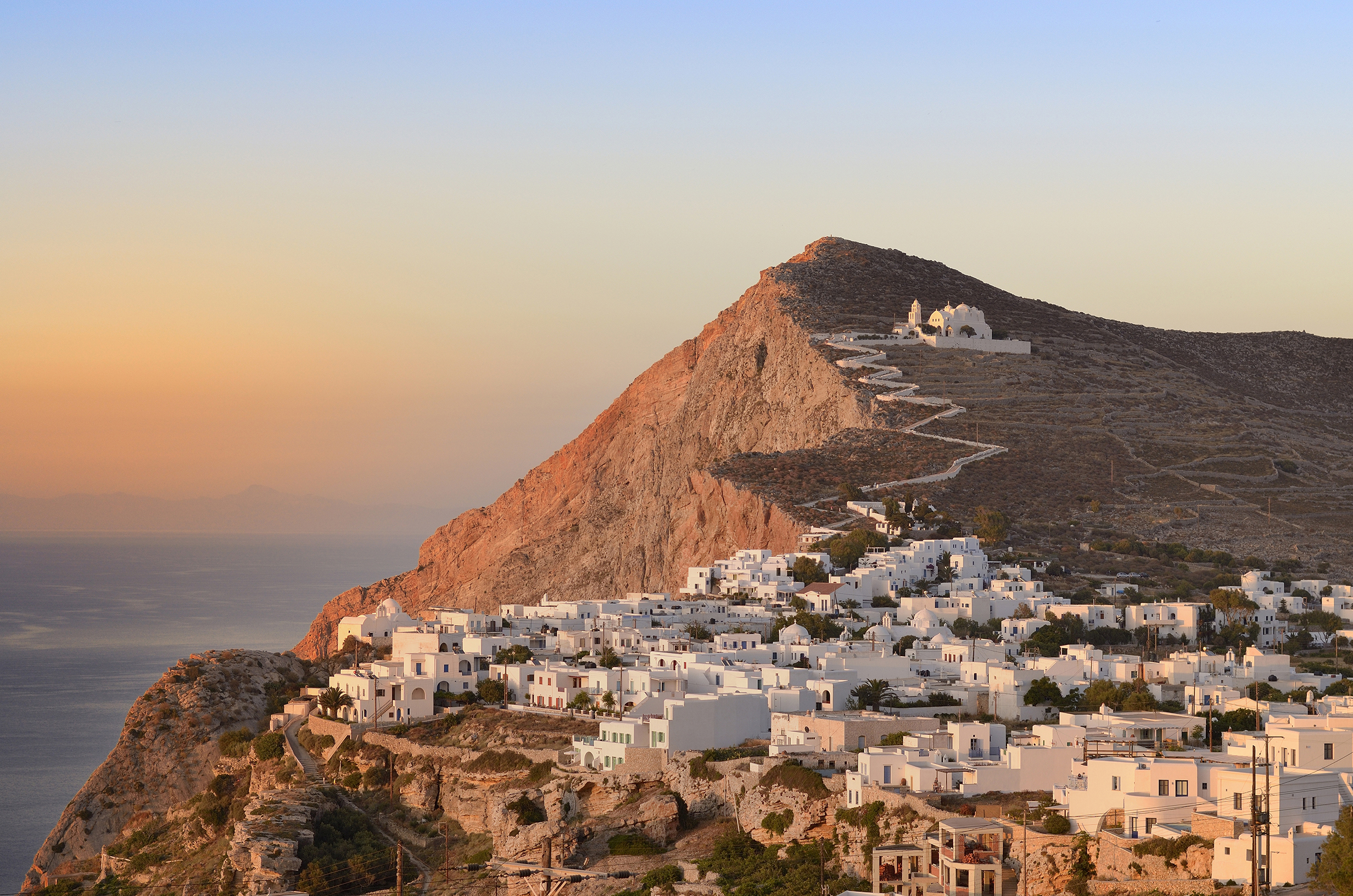 Whitewashed buildings of a town on Folegandros at sunset with a white pathway weaving up the hill behind