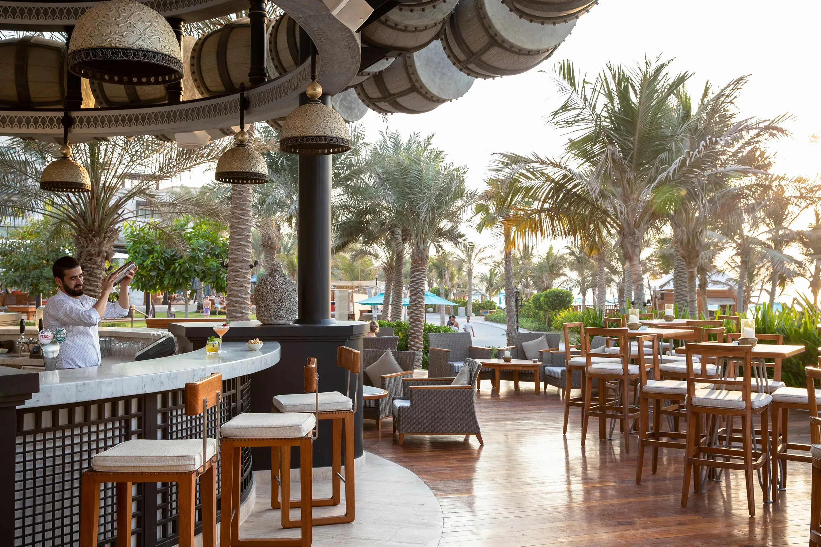 Open‑air beachfront bar at Jumeirah Al Naseem Dubai featuring elegant wooden seating, decorative lanterns and views of palm‑lined pathways.