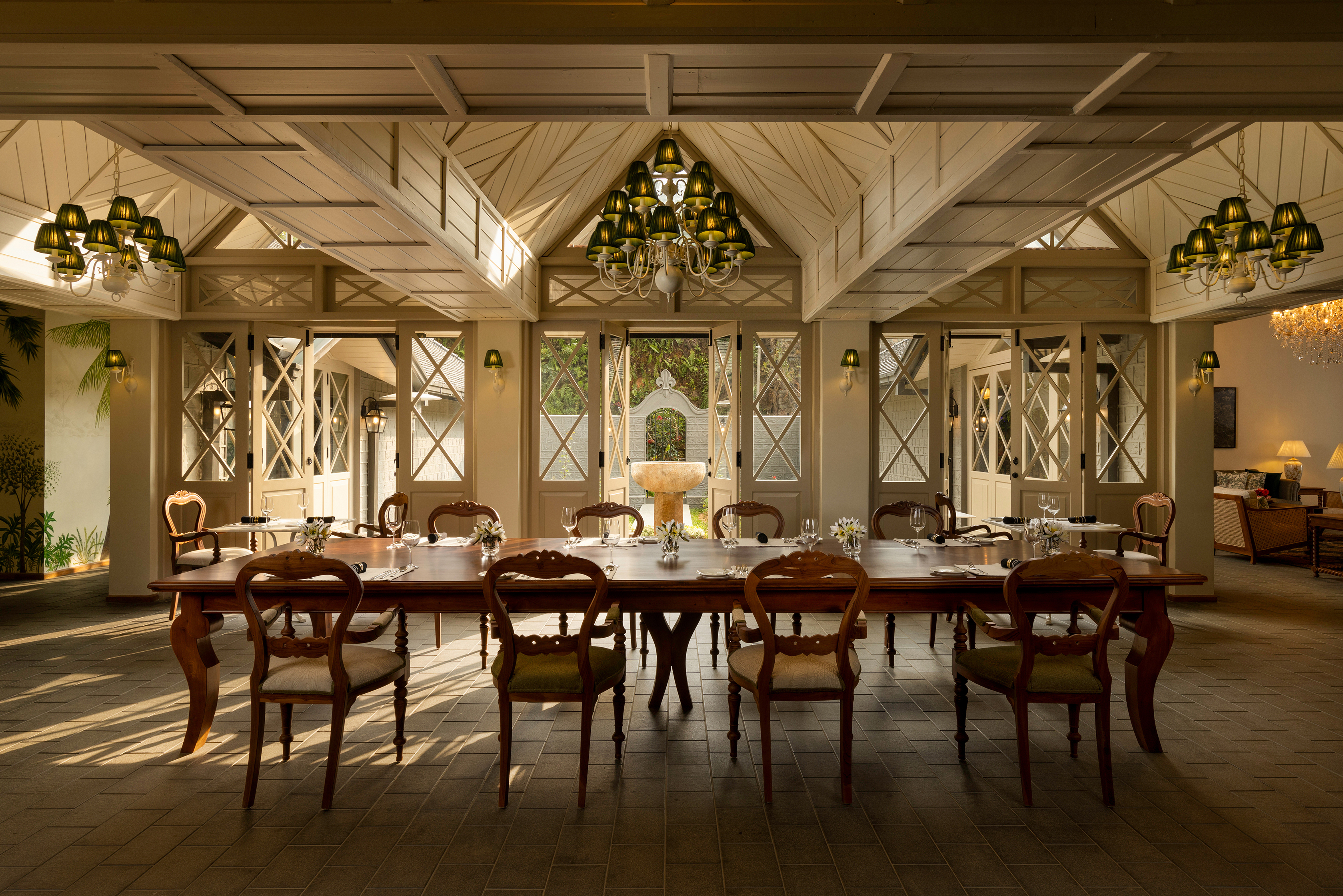 An ornate dining room at Uga Halloowella featuring a long table set for a meal beneath patterned wood panelled ceilings and set before three large doors leading outside