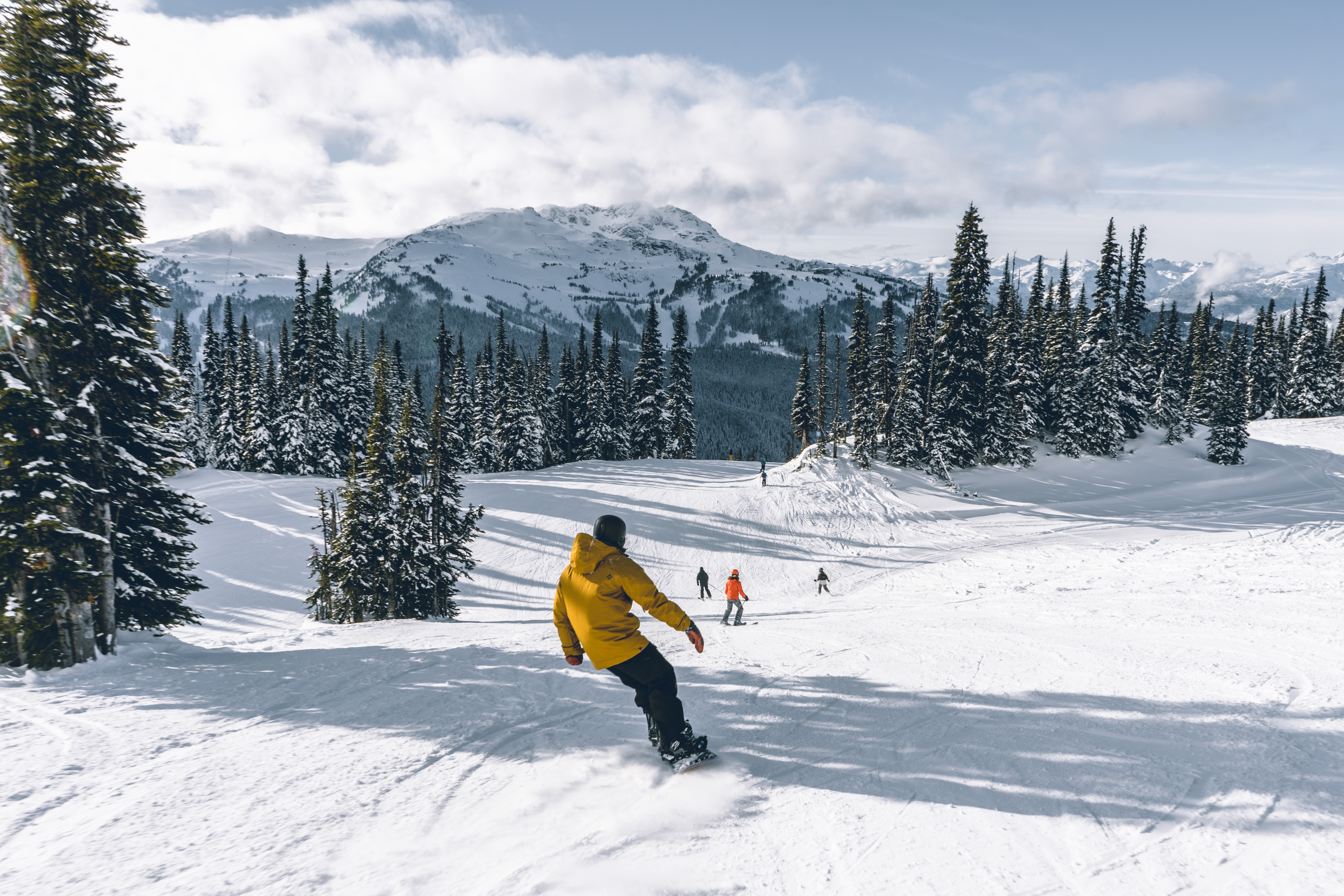 A snowboarder heading down slope with skiers ahead