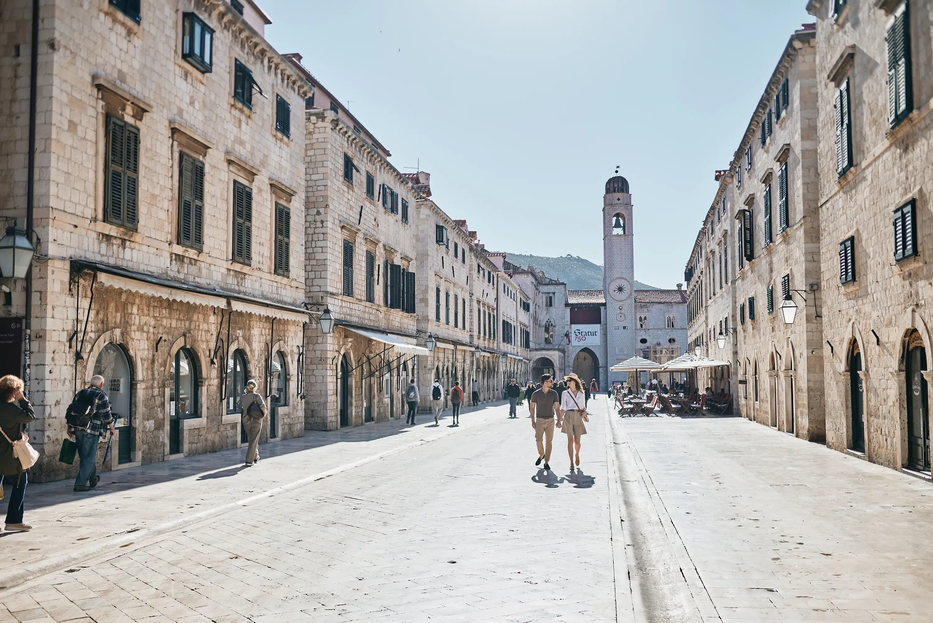 Two people strolling up a street in Dubrovnik Old Town surrounded by old stone buildings and other people
