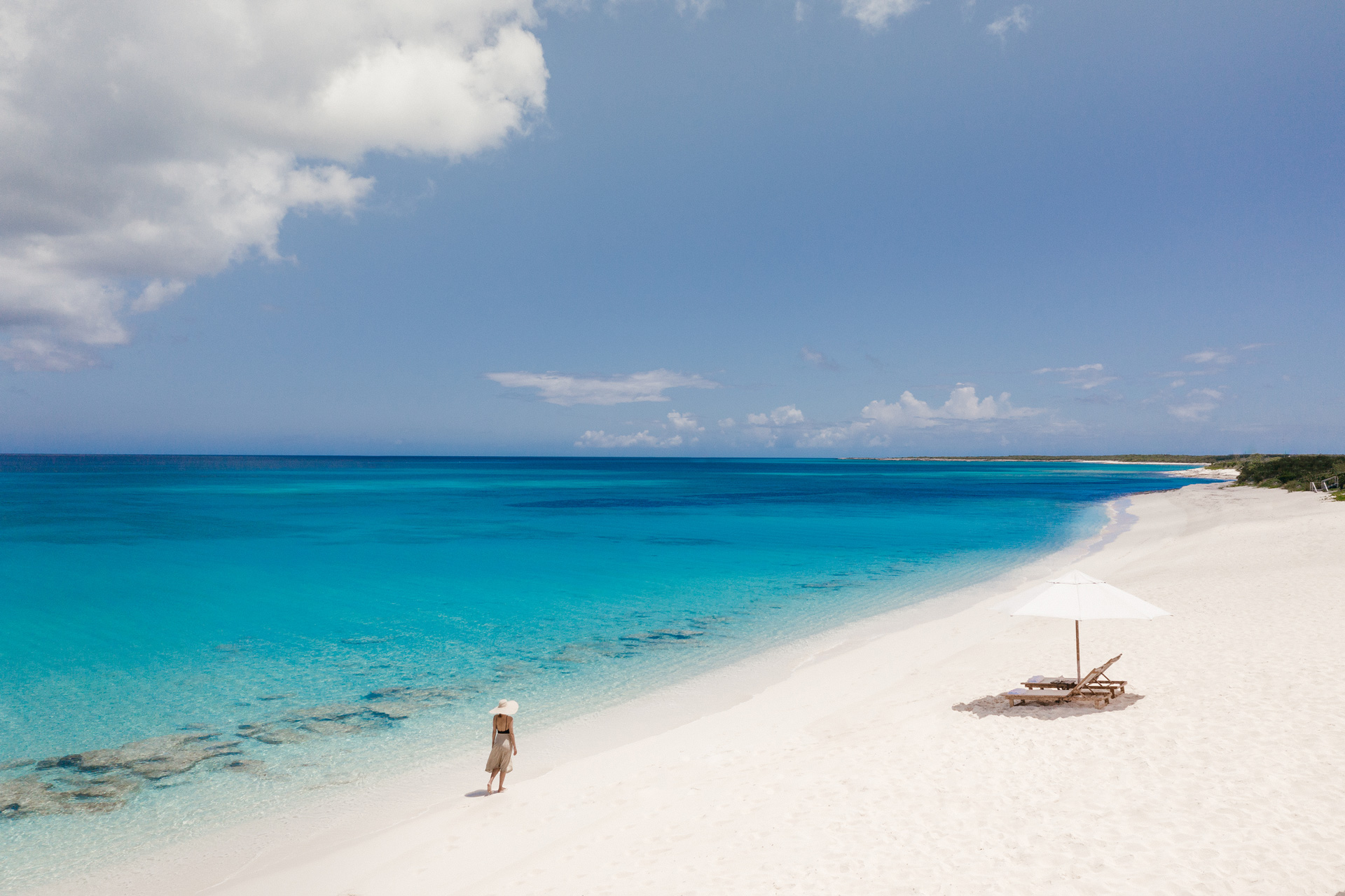 A woman stands on a sandy beach near two sun loungers