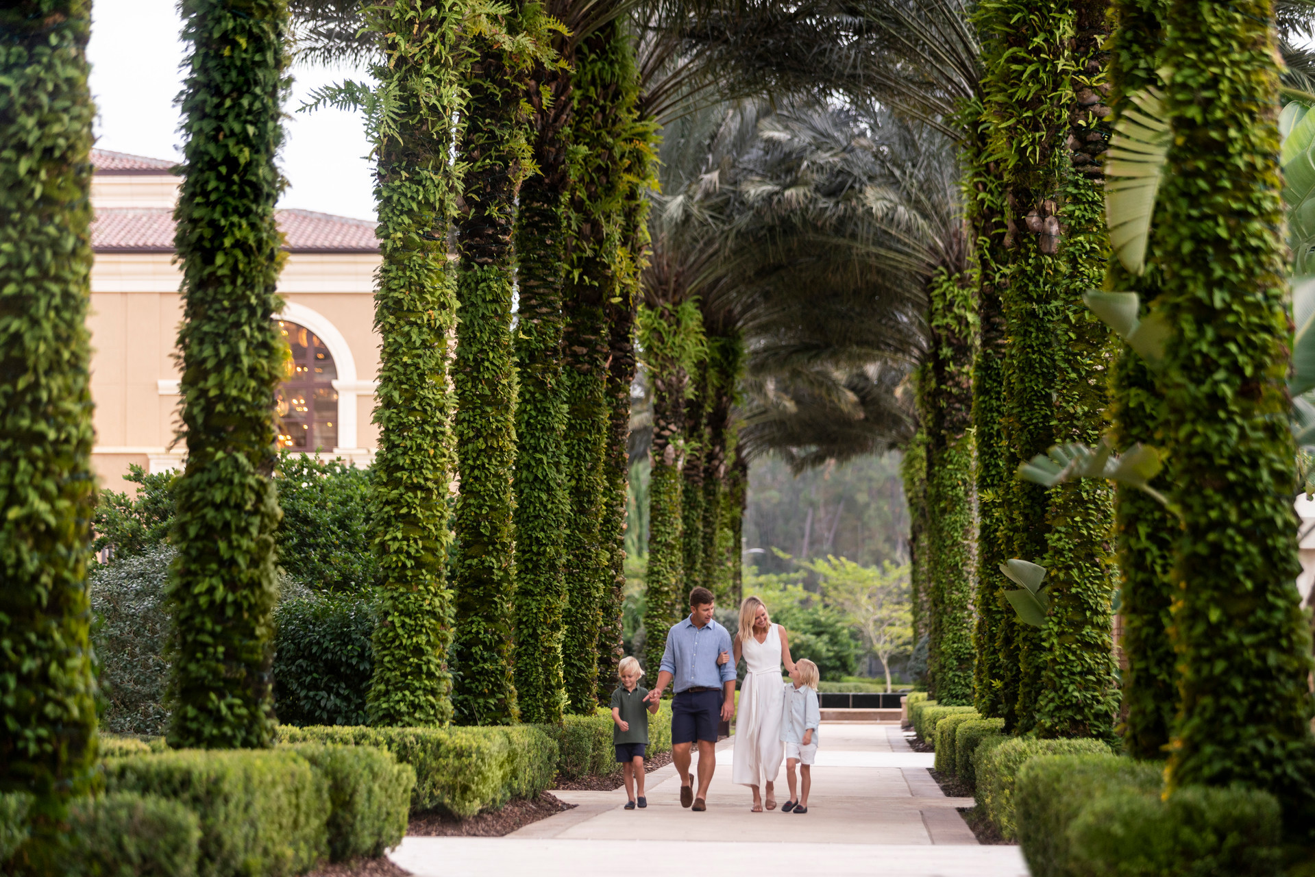 Family of four walking together through a palm-lined path at  Four Seasons Resort Orlando at Walt Disney World® Resort