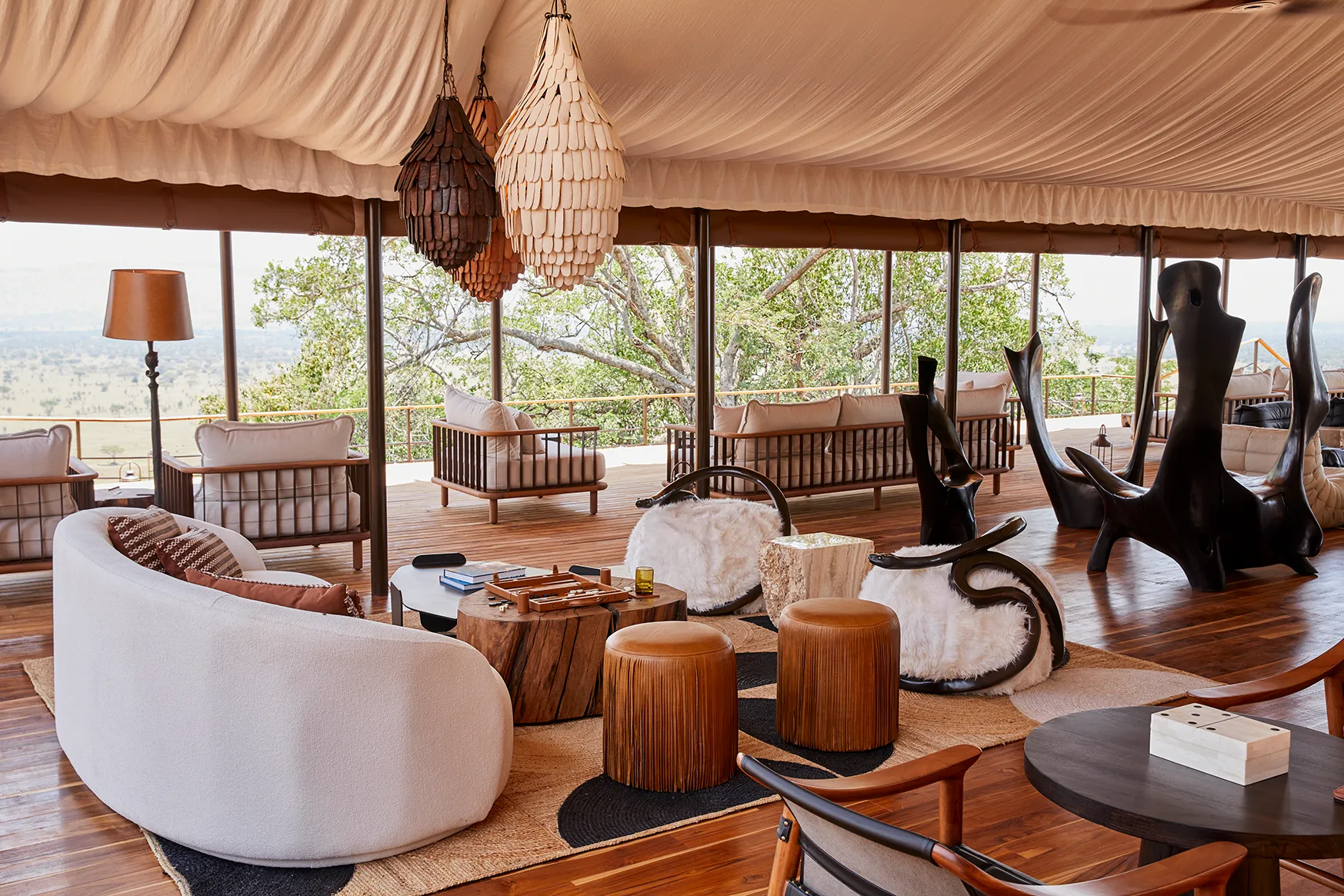 Spacious safari lodge lounge with curved seating, sculptural furniture, pendant lights, and panoramic savannah views.