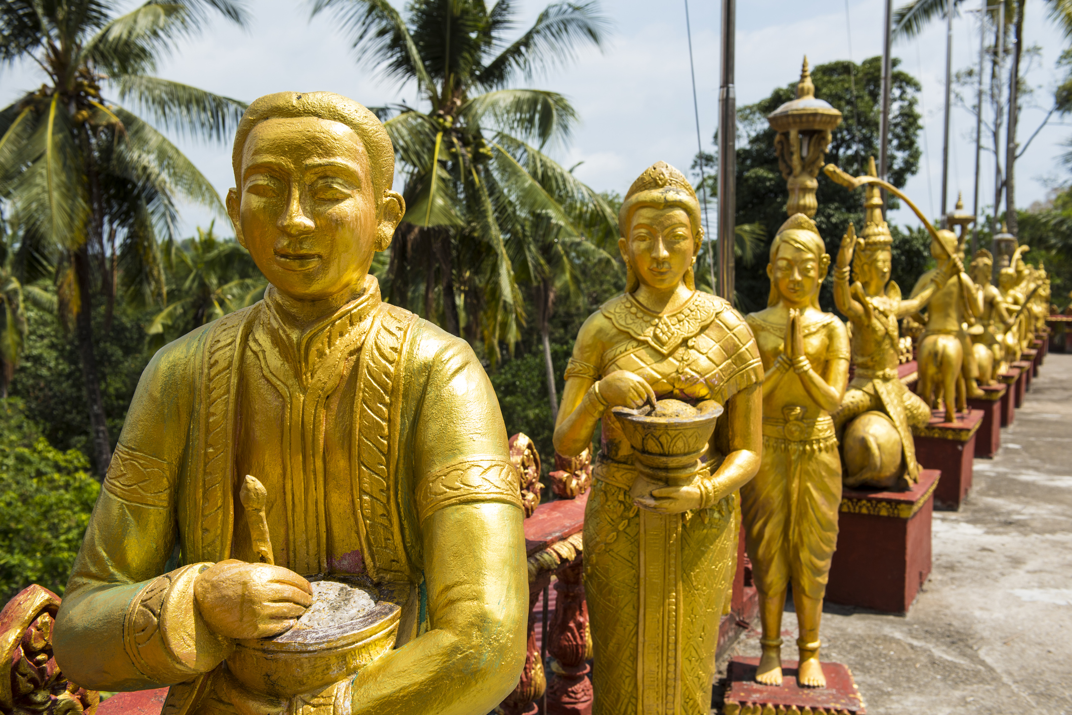 A row of golden statues along a pathway lined with palm trees.