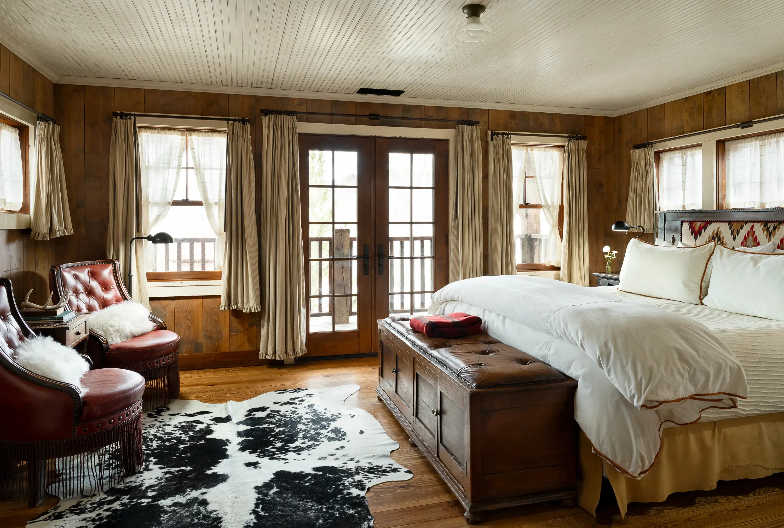 Elite Granite Lodge room at The Ranch at Rock Creek in Montana featuring a cow print rug, plush ranch-style furniture, and pale soft furnishings with surrounded by lots of windows and french doors to a balcony
