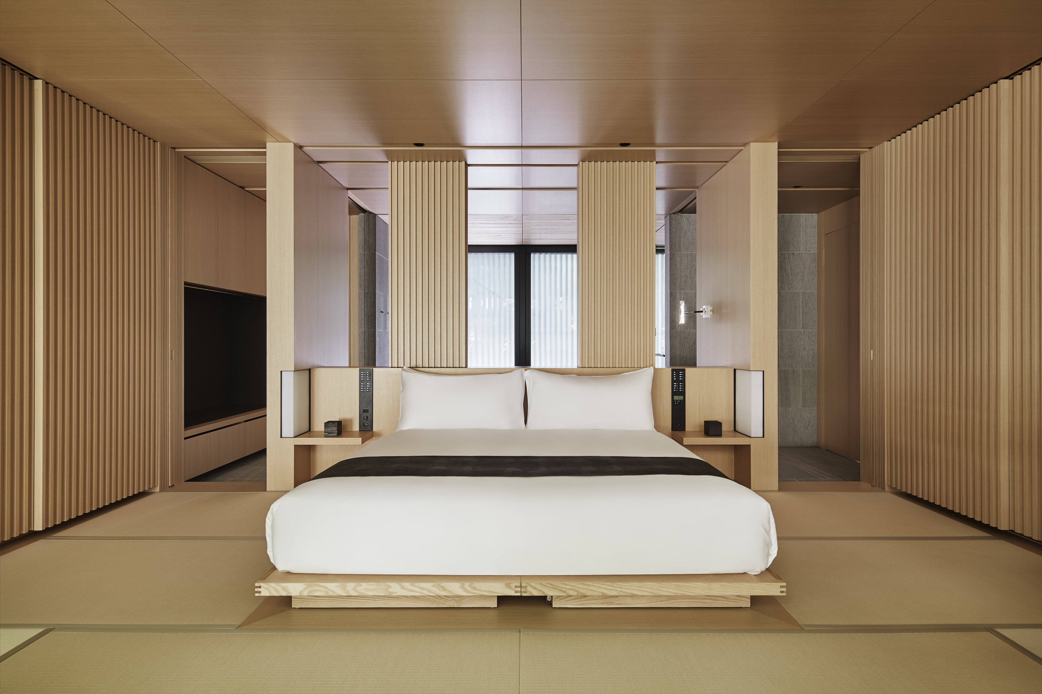 A comfy bed in a suite at Aman Kyoto surrounded by pale wood decor 