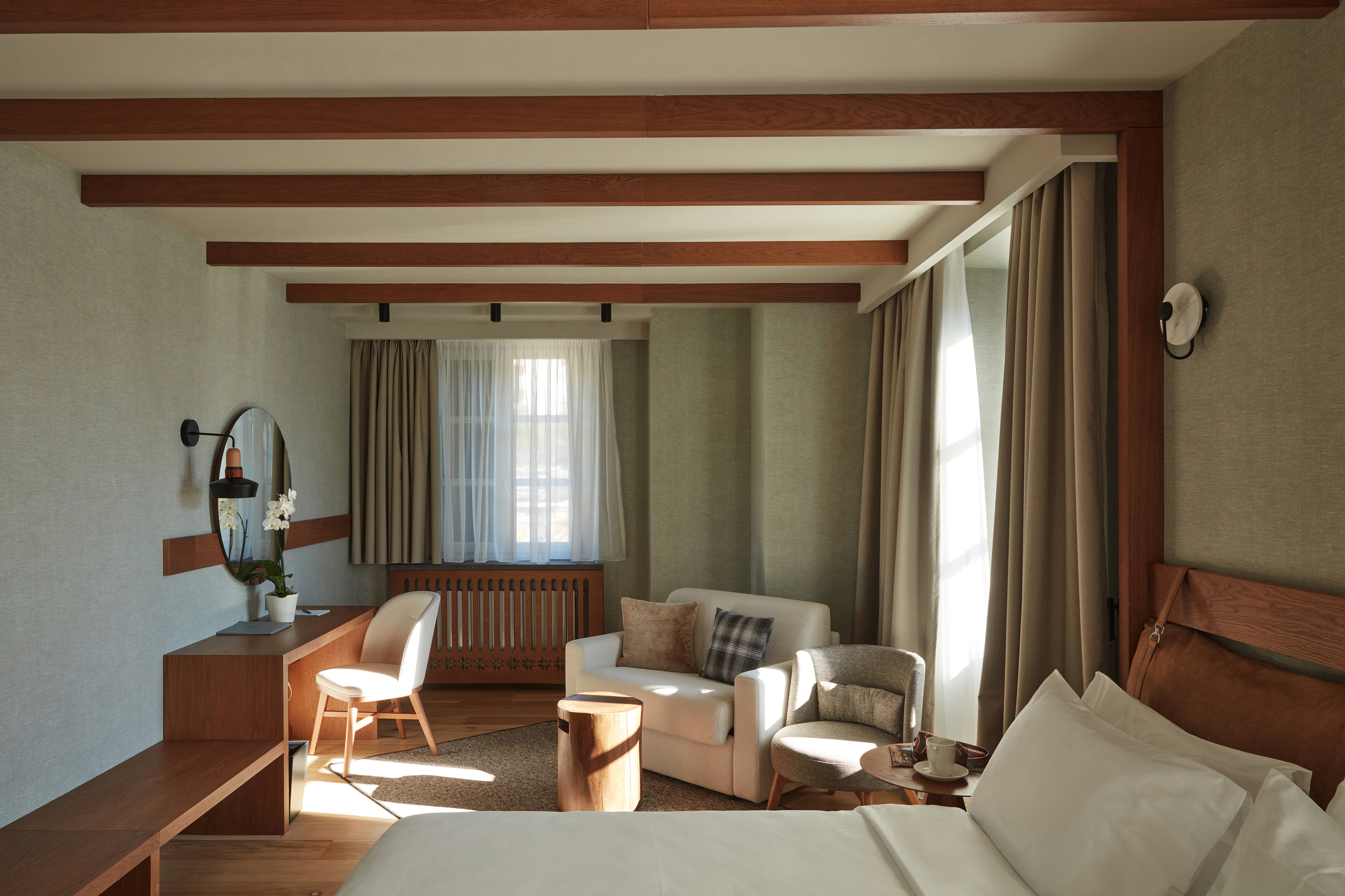 A cosy chalet-style bedroom decorated in neutral tones with a desk area, comfy seating and a glimpse of a bed