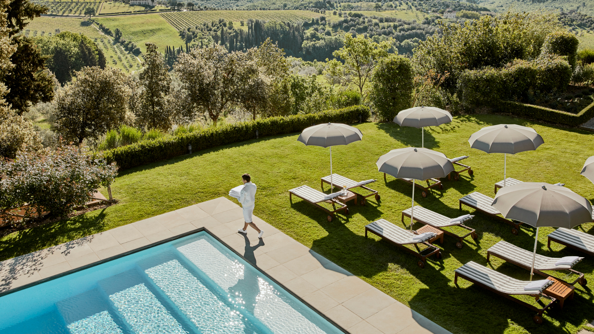 An aerial view of a pool and loungers with Tuscany landscape in the distance