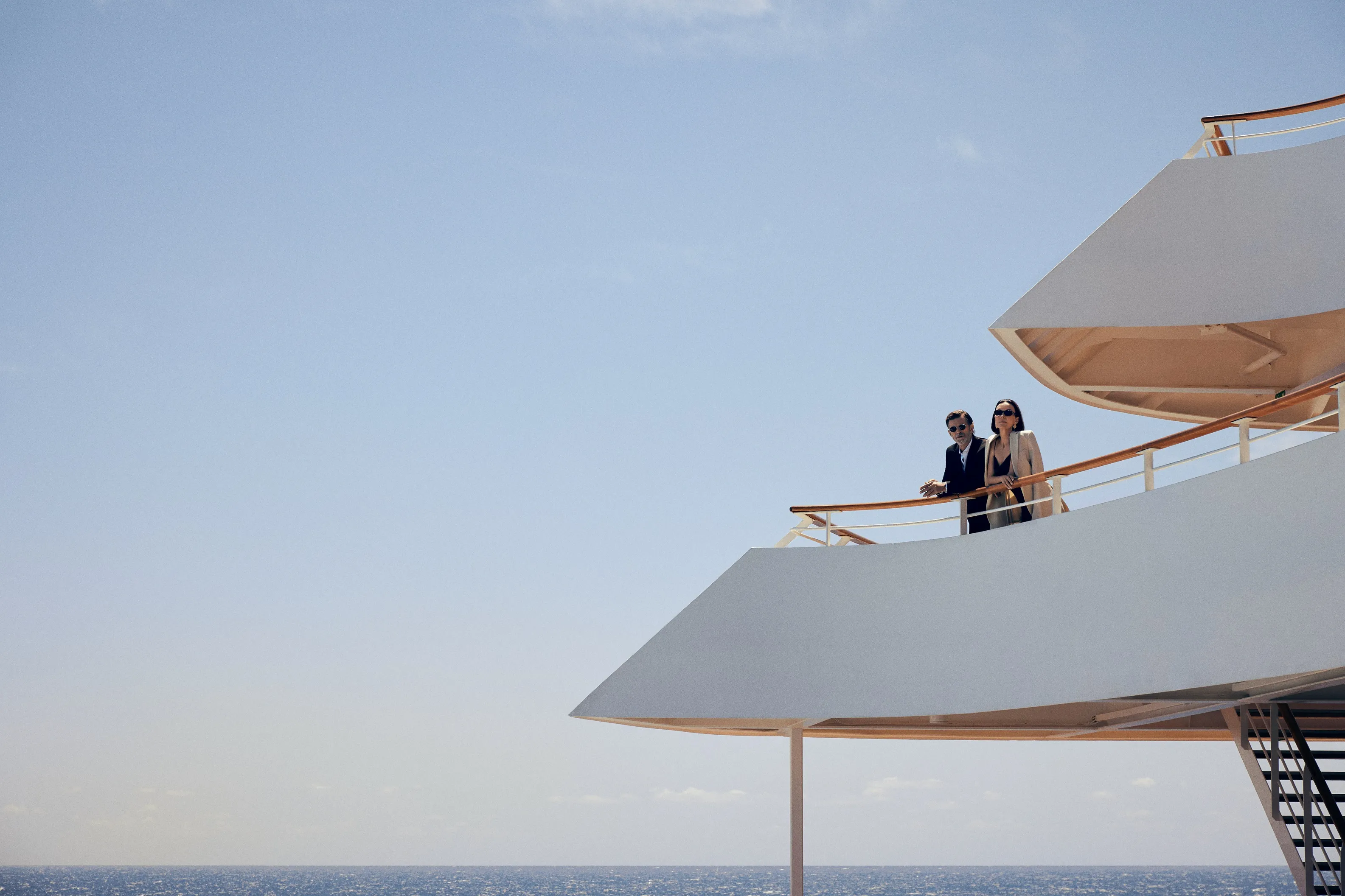 Two people standing on a sleek Crystal cruise ship deck, gazing out at the ocean beneath a clear blue sky.